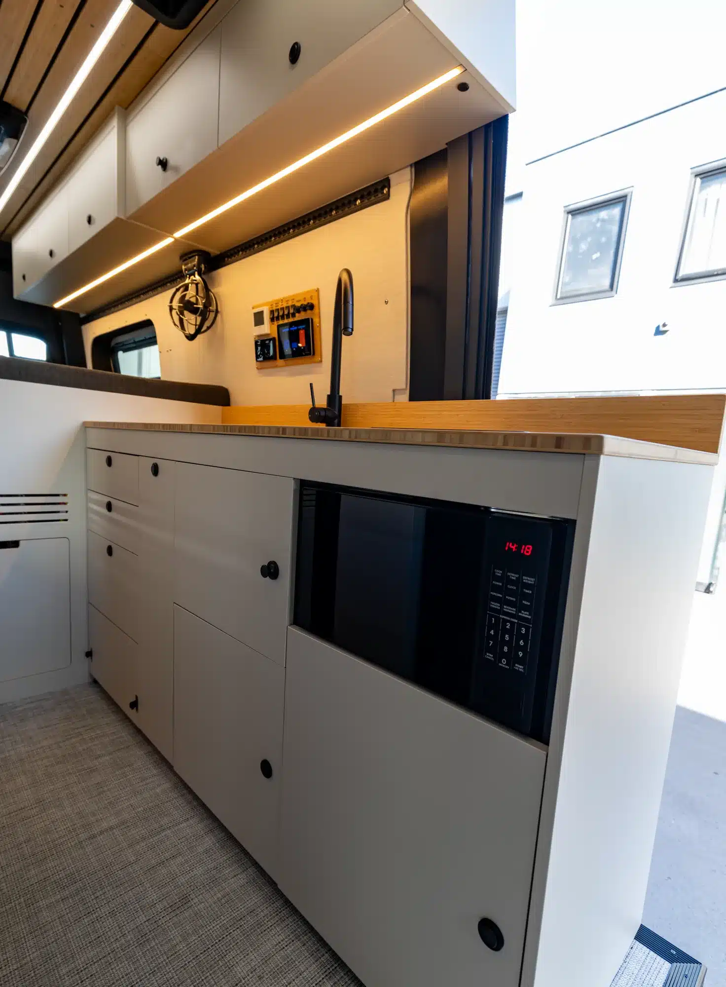 Innenansicht der Küchenzeile im SUMMIT L1 Offroad-Reisemobil mit Spüle, Mikrowelle, Stauraum und LED-Beleuchtung