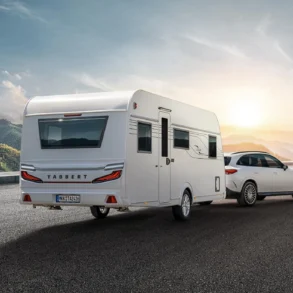 TABBERT Cazadora Wohnwagen wird von einem weißen Kombi auf einer Straße vor Bergkulisse gezogen