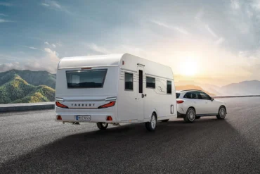 TABBERT Cazadora Wohnwagen wird von einem weißen Kombi auf einer Straße vor Bergkulisse gezogen