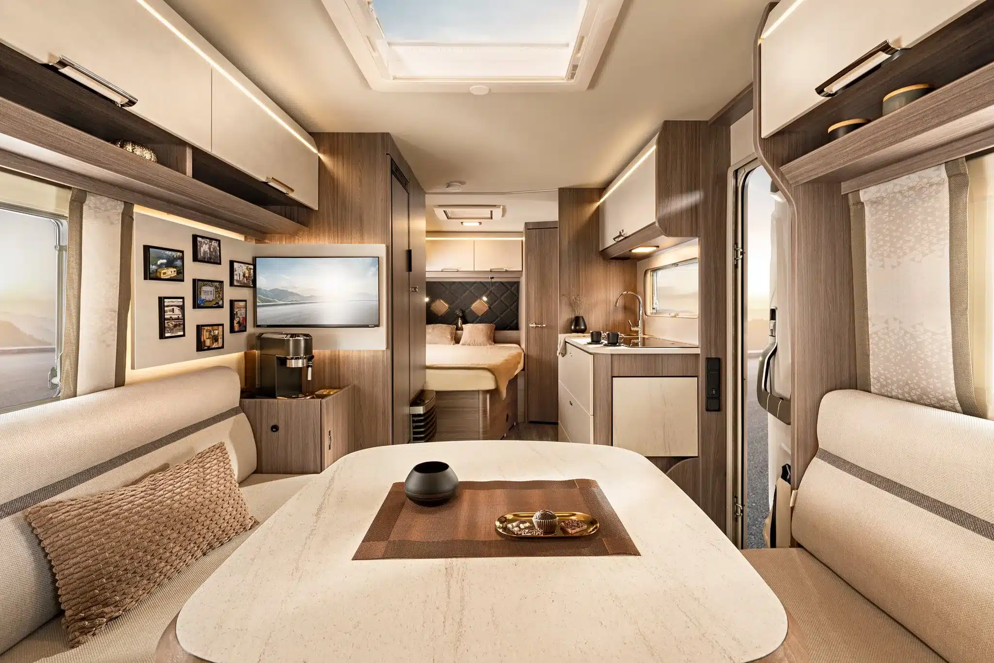 Innenansicht des TABBERT Cazadora Wohnwagens mit heller Sitzgruppe, Fotowand, Kaffeemaschine, moderner Küche und Schlafbereich