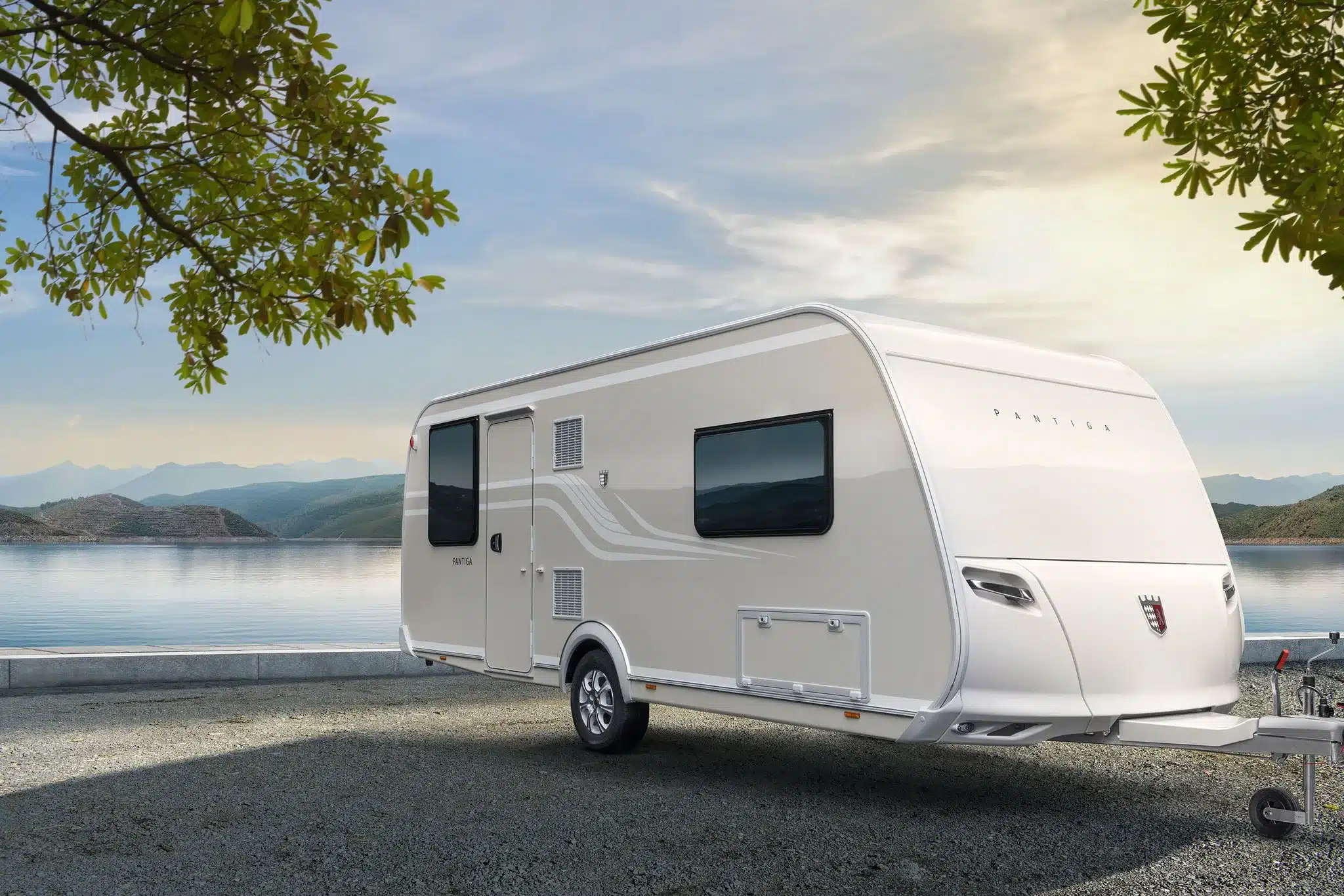 Tabbert Pantiga Finest Edition Wohnwagen steht am Ufer eines Sees mit Bergen im Hintergrund