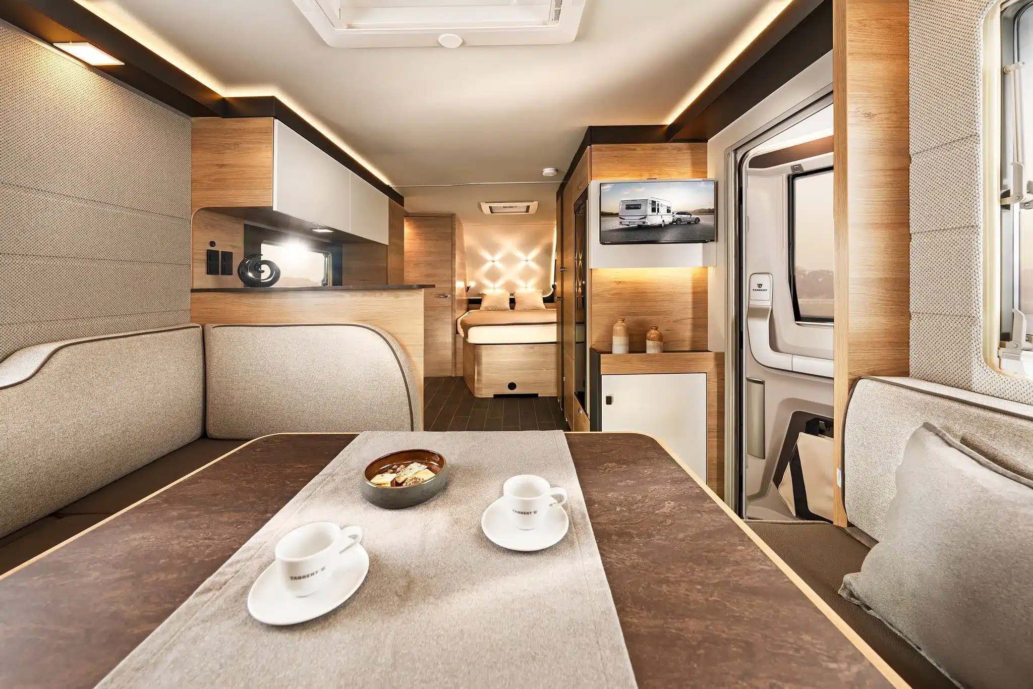 Blick in den stilvollen Innenraum eines Tabbert Pantiga Finest Edition Wohnwagens mit Sitzgruppe, Küche und Bett