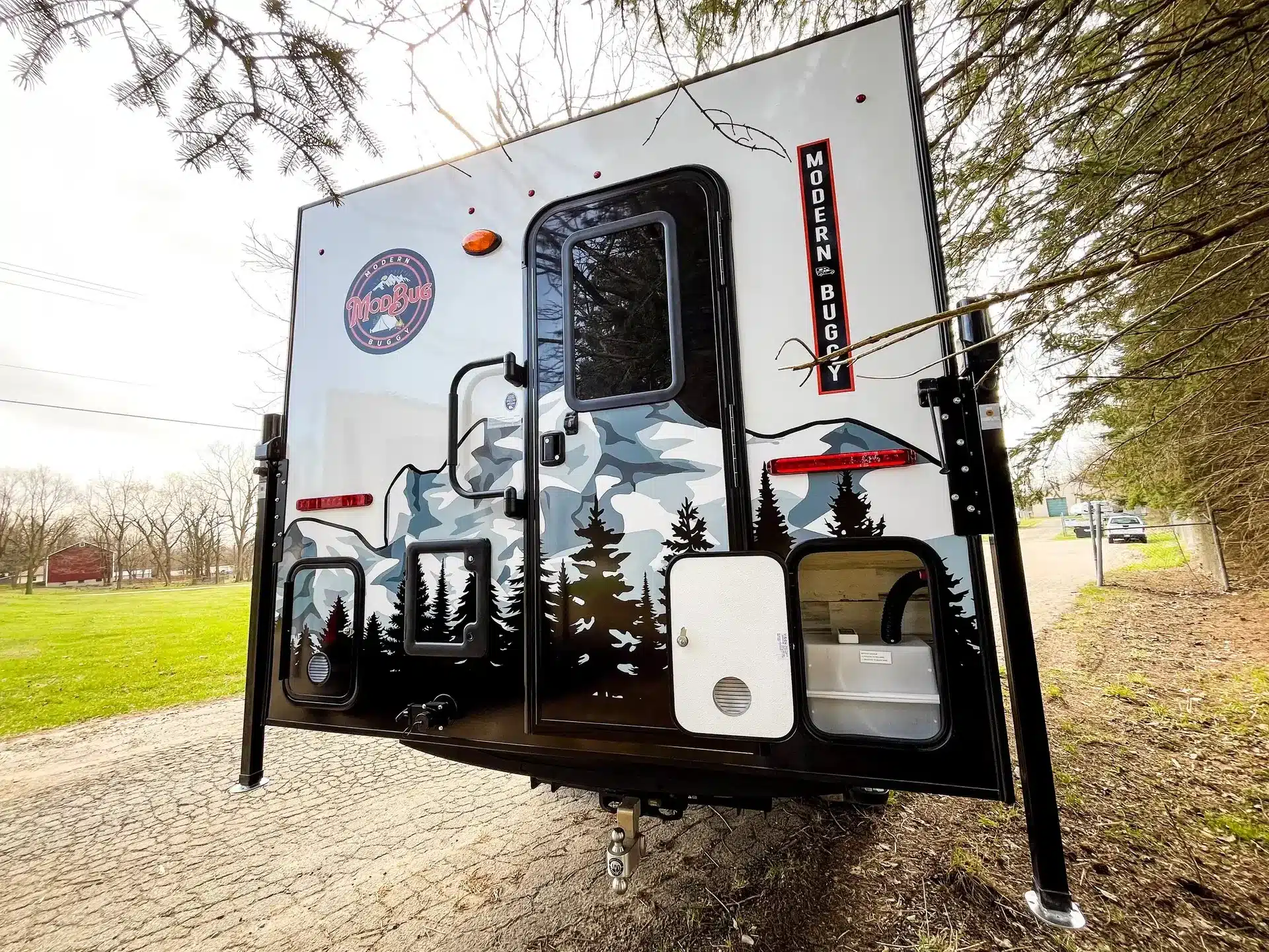 Frontansicht des Modern Buggy TC14 Truck Campers mit markantem Design und Outdoor-Grafik, aufgestellt im Grünen.