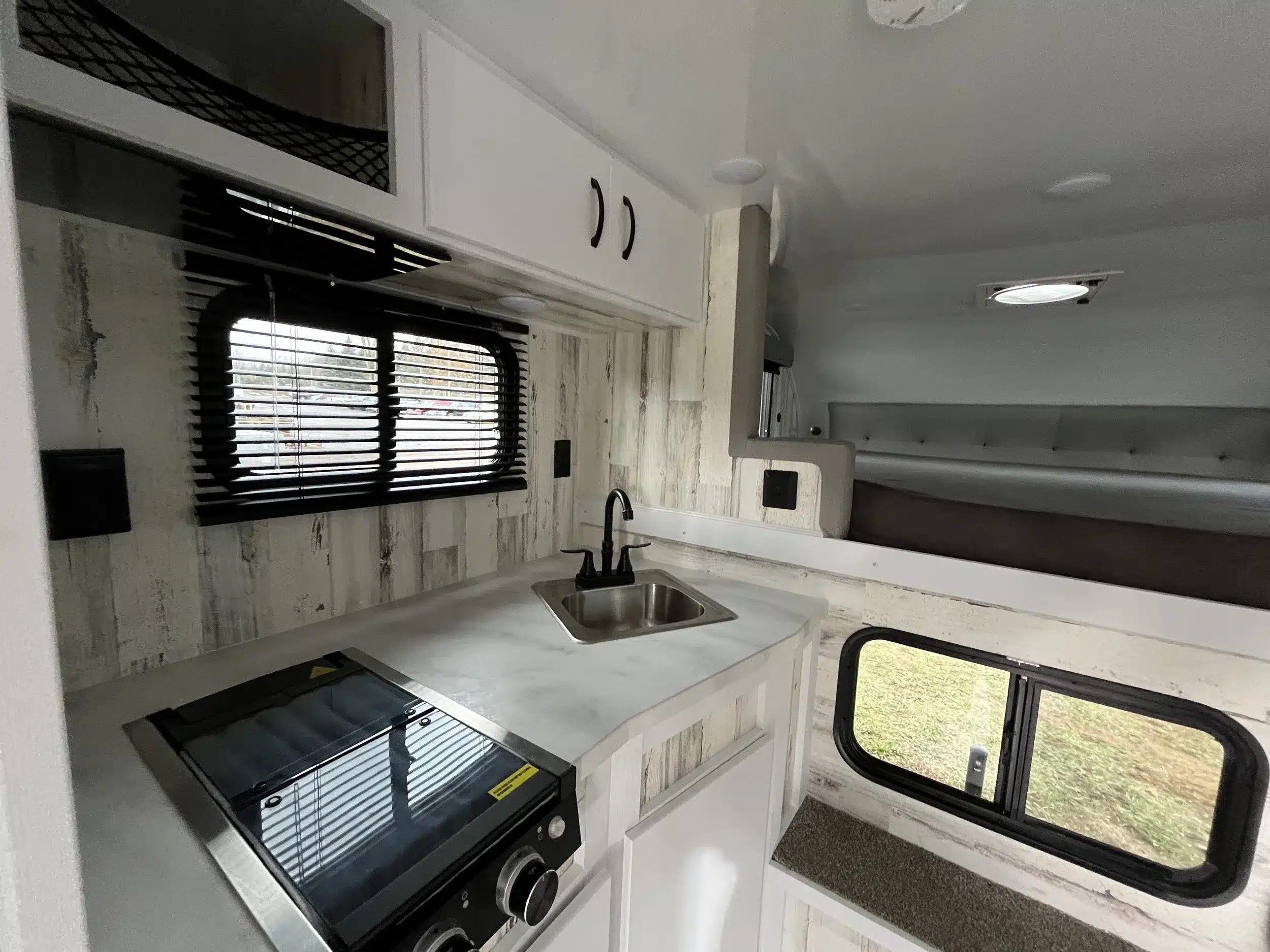 Blick auf die Küchenzeile mit Herd, Spüle und Schlafbereich im TC14 Truck Camper von Modern Buggy RV