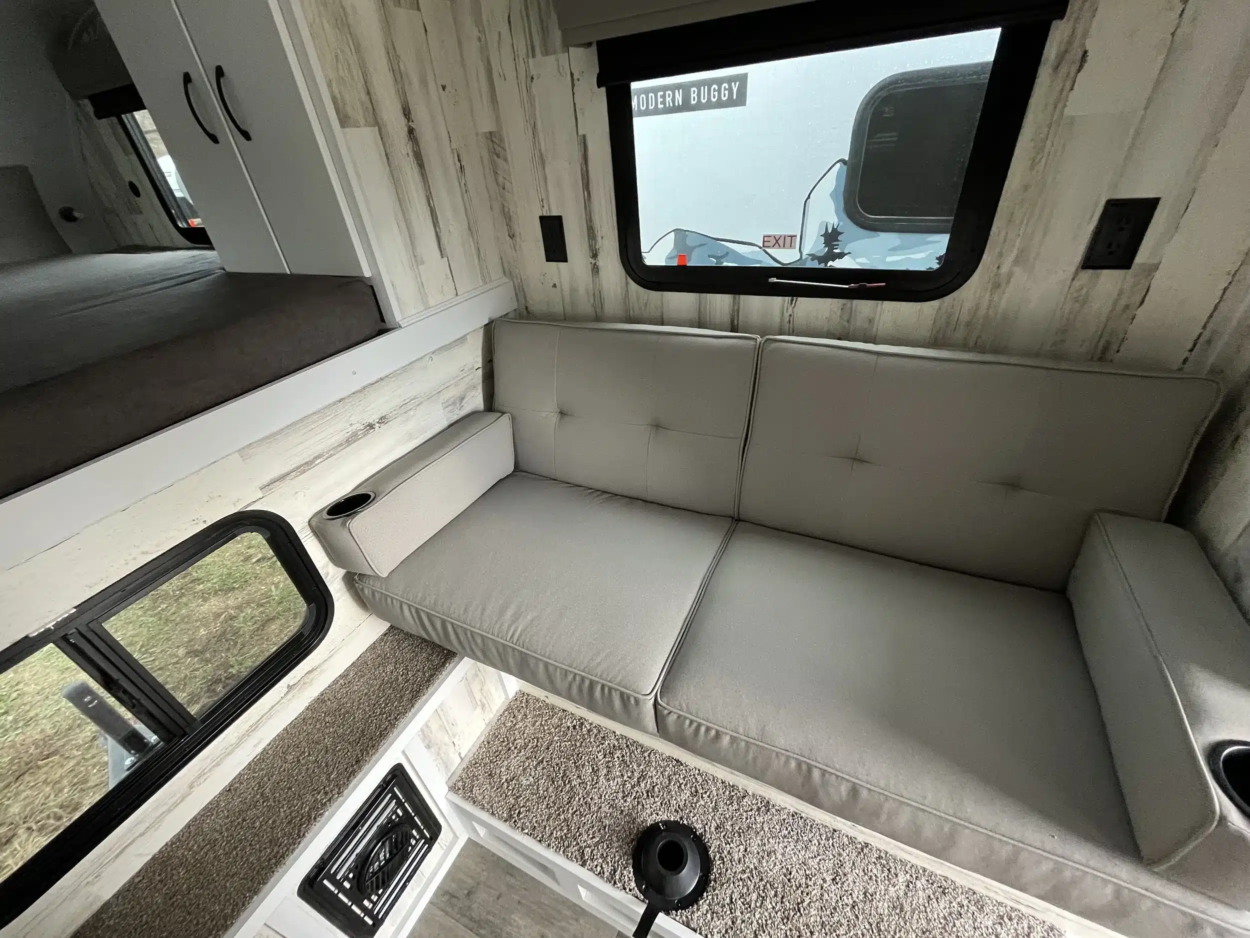 Sitzbereich mit grauem Sofa, Fenster und Stauraum im TC14 Truck Camper von Modern Buggy RV