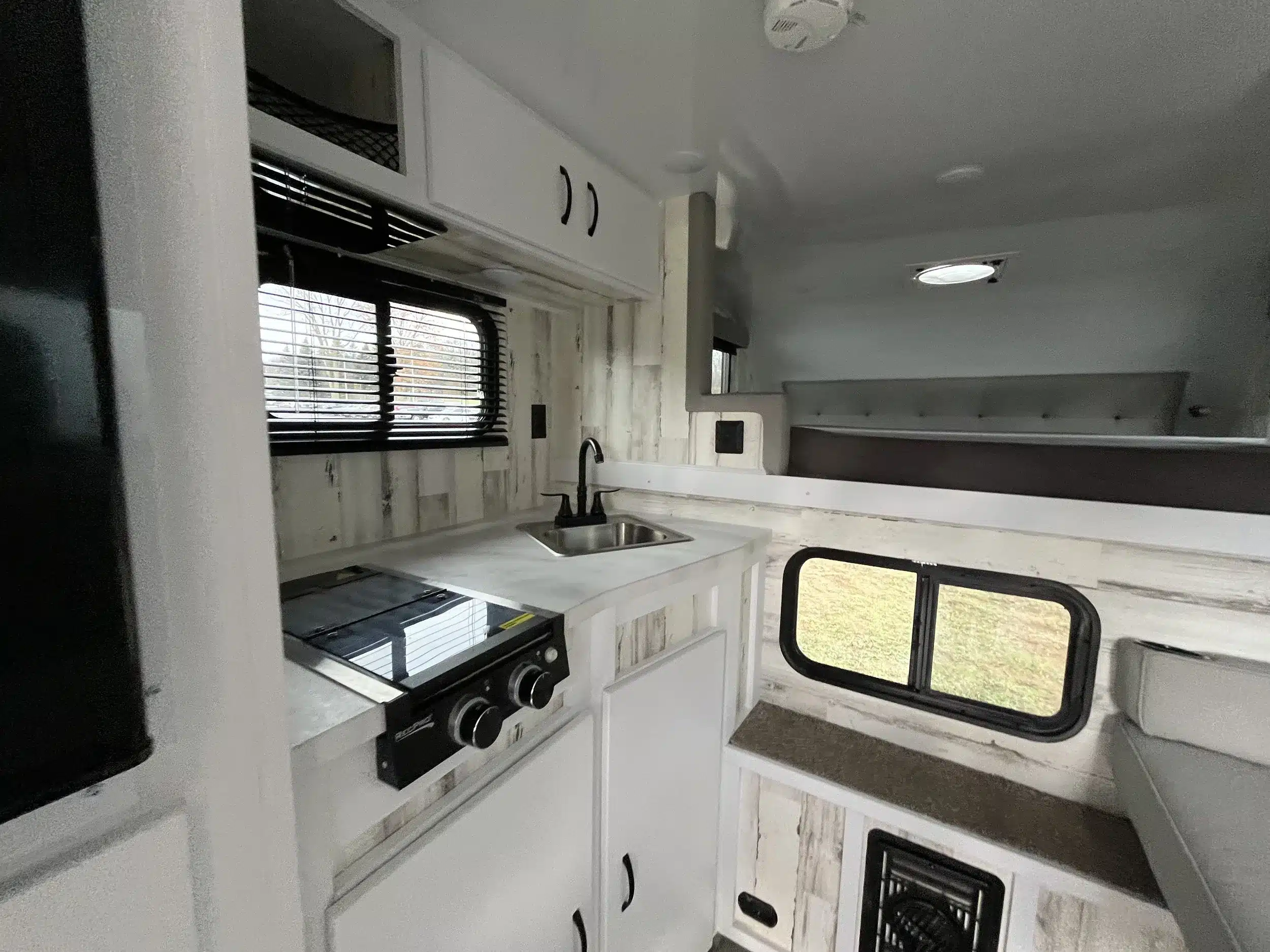 Blick in den Innenraum eines TC14 Truck Campers mit Küchenzeile, Herd, Spüle, Fenster und Schlafbereich