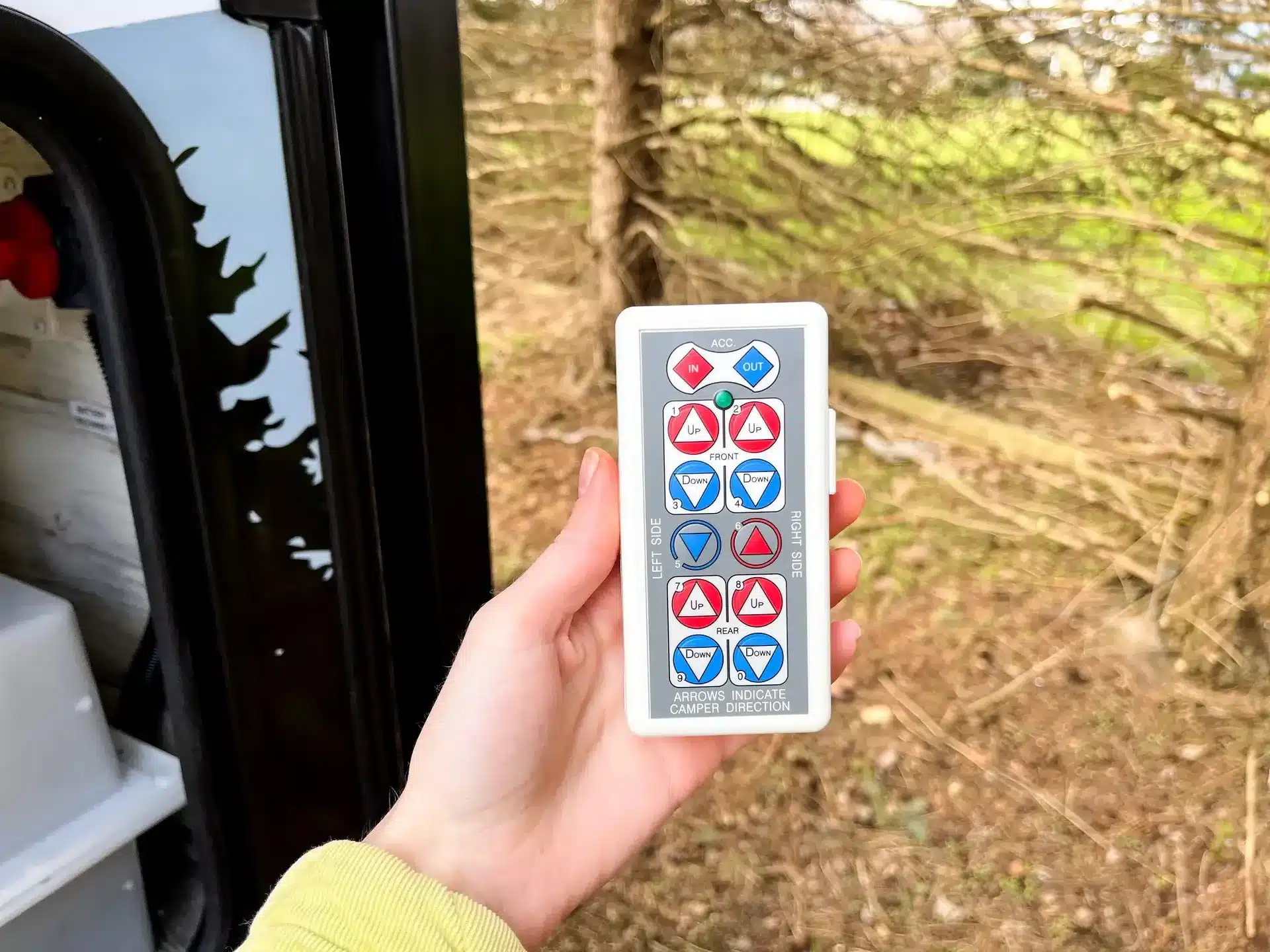 Hand hält Fernbedienung zur Steuerung der Stützen eines Truck Campers im Freien