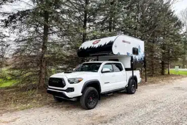 Weißer Pickup mit aufgesetztem Modern Buggy RV TC9 Truck Camper steht auf Waldweg