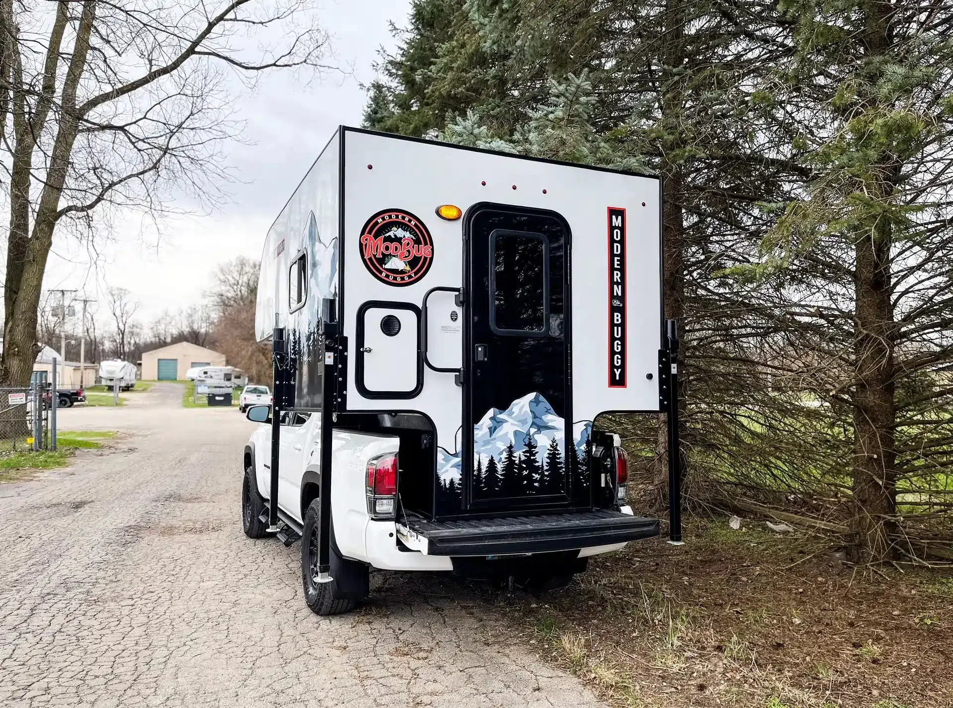 Heckansicht eines Modern Buggy TC9 Truck Campers auf einem weißen Pickup, geparkt am Waldrand