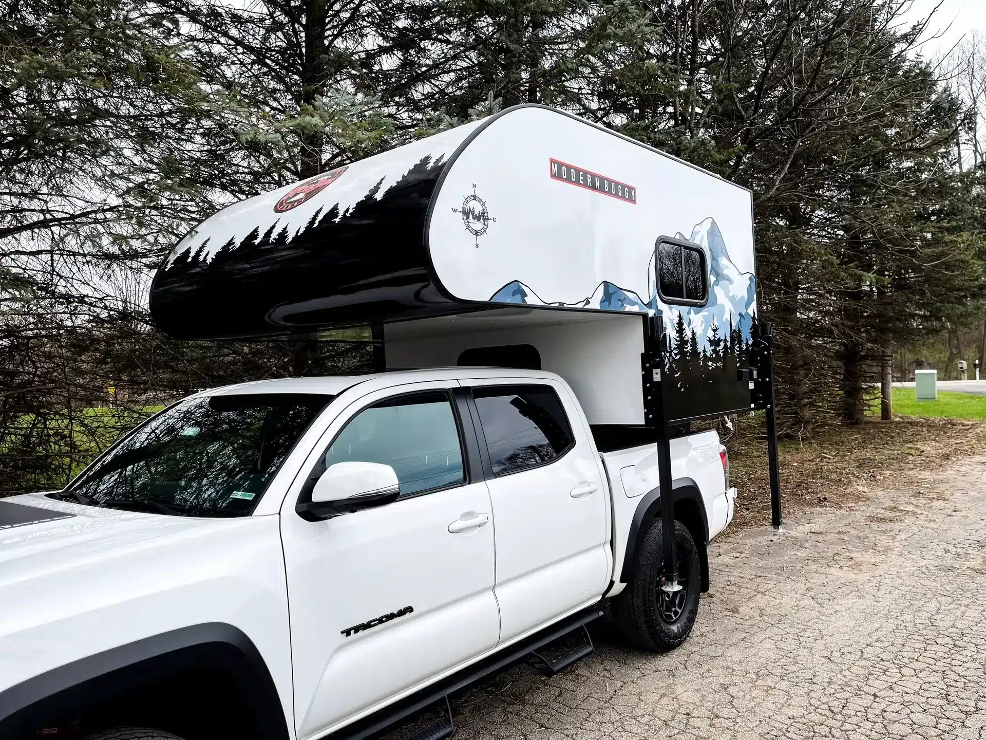 Modern Buggy TC9 Truck Camper montiert auf einem weißen Pickup-Truck, geparkt am Waldrand.
