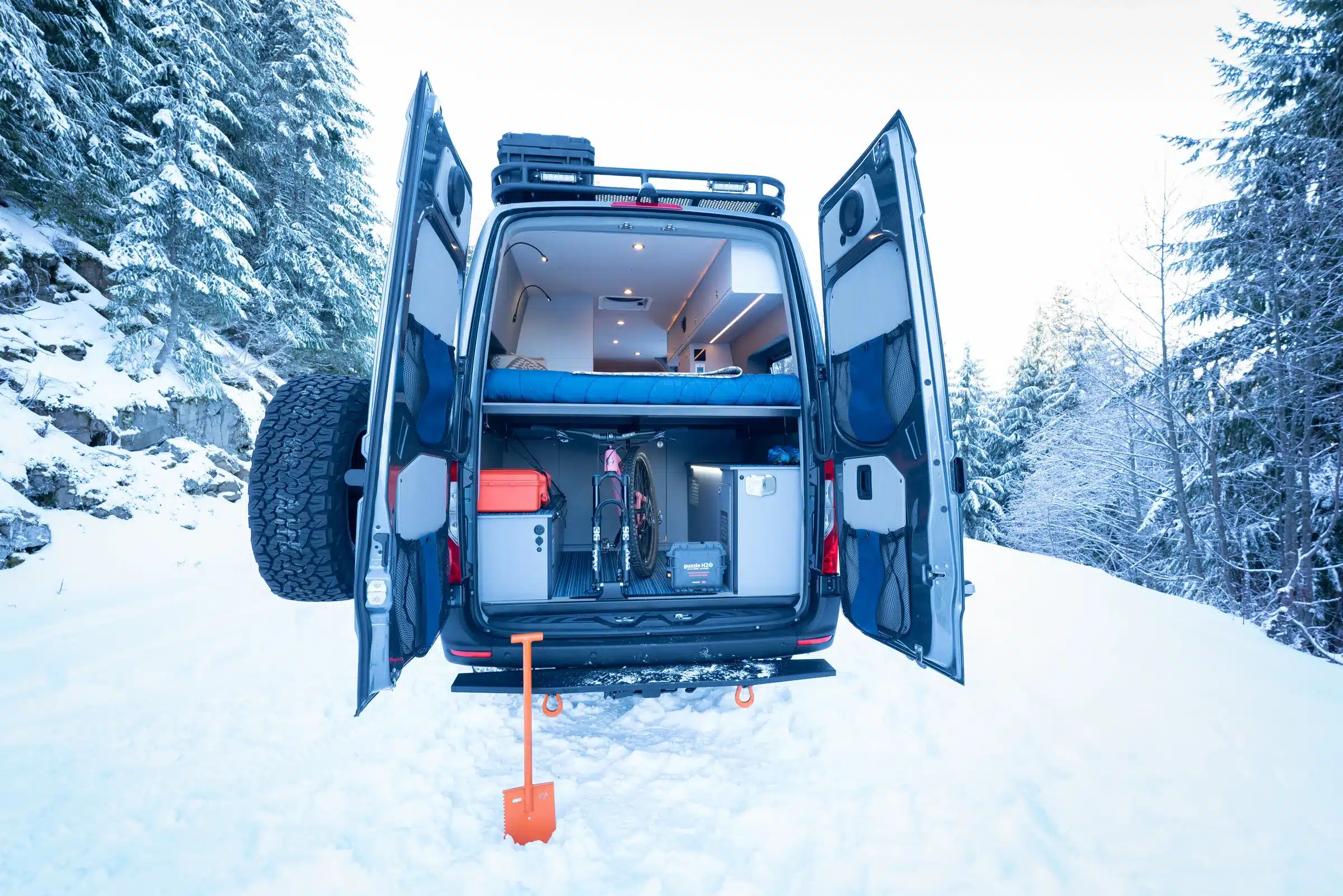 Geöffnete Hecktüren eines Mercedes Sprinter 170 4x4 Campervans im Schnee, Blick auf Stauraum, Fahrrad und Innenausbau