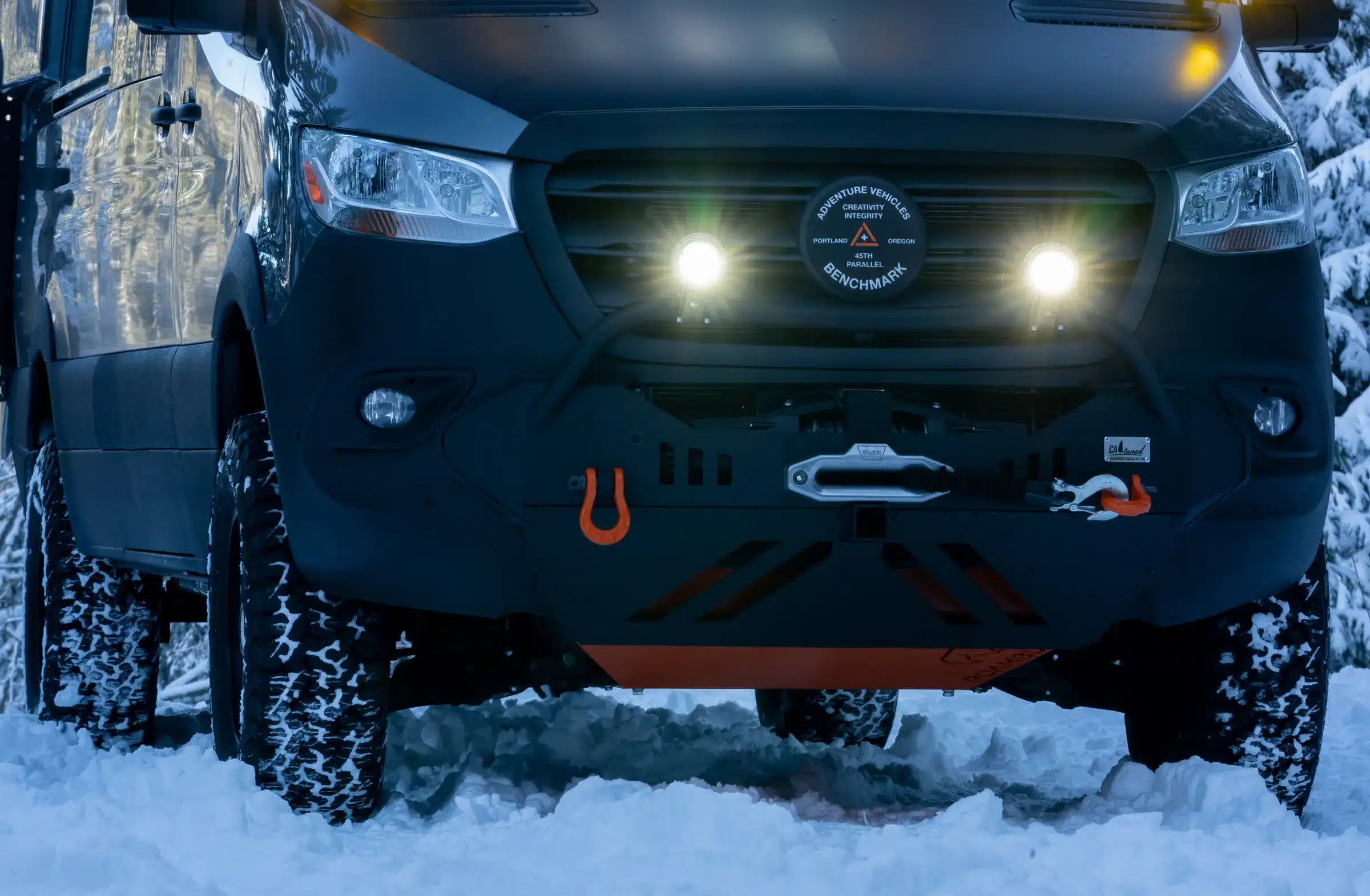 Nahaufnahme der Front eines ausgebauten Mercedes Sprinter 170 4x4 mit Offroad-Stoßfänger, Zusatzscheinwerfern und Schneebedeckten Reifen