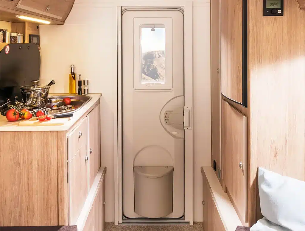 Blick in den Innenraum einer Tischer Trail/Box 280 Wohnkabine mit Küchenzeile, Herd, Spüle und Eingangstür