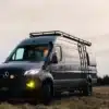 Tralfamadore 4x4 Sprinter Camper mit Dachträger und Leiter auf einer Wiese