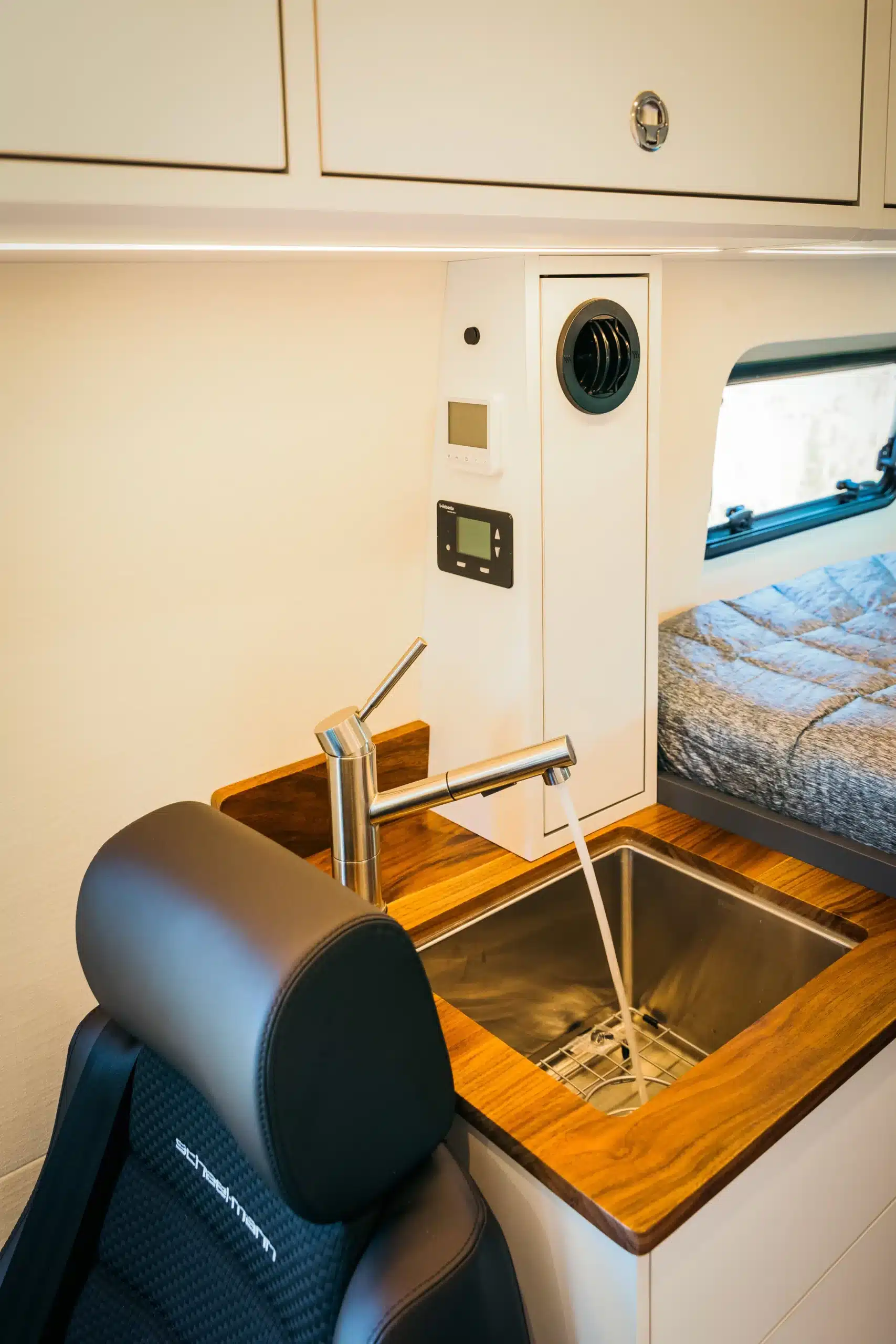 Edelstahl-Spülbecken mit moderner Armatur im Tree House Sprinter 4x4 Campervan, daneben ein Scheel-Mann Sitz und Bedienelemente