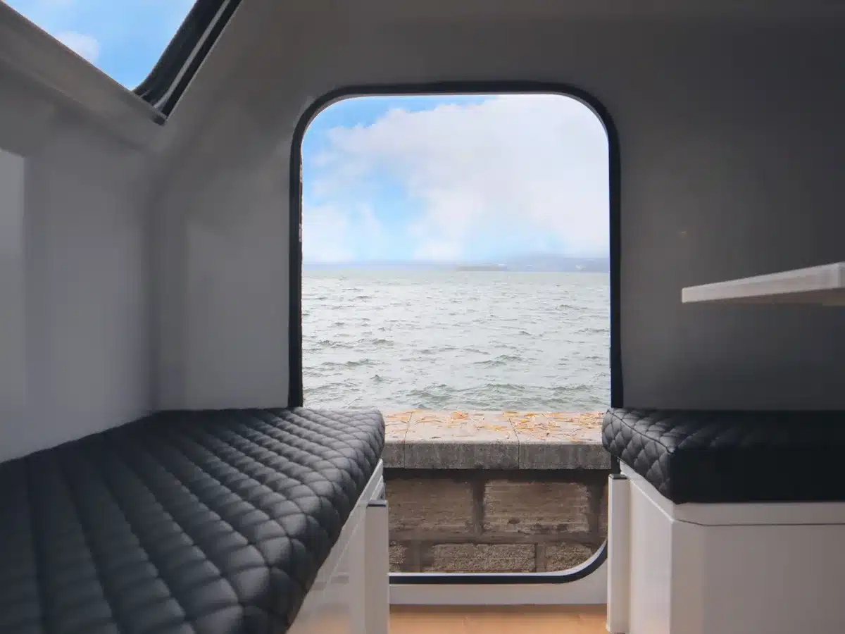 Blick aus dem Innenraum eines Offroad-Caravans Valkari X1 durch die offene Tür auf Wasser und Himmel