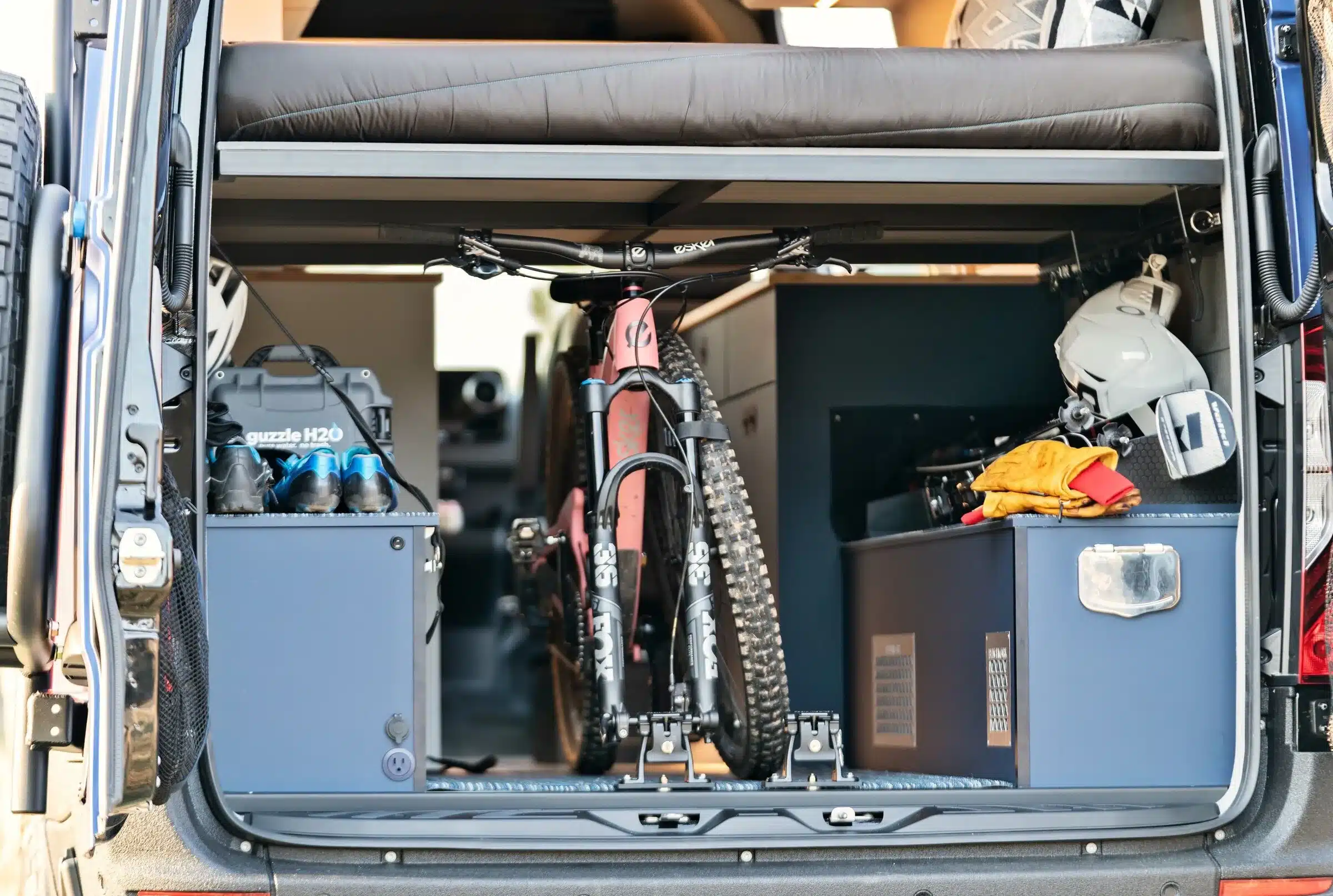 Blick in die Heckgarage eines ausgebauten Mercedes Sprinter 4x4 mit Fahrrad, Ausrüstung und Stauboxen