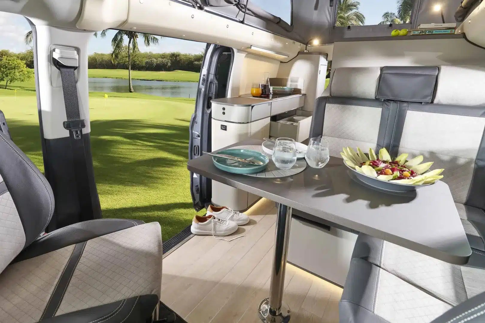 Innenansicht des Westfalia Jules Verne Campervans mit Tisch, Sitzbank, Küche und Blick ins Grüne