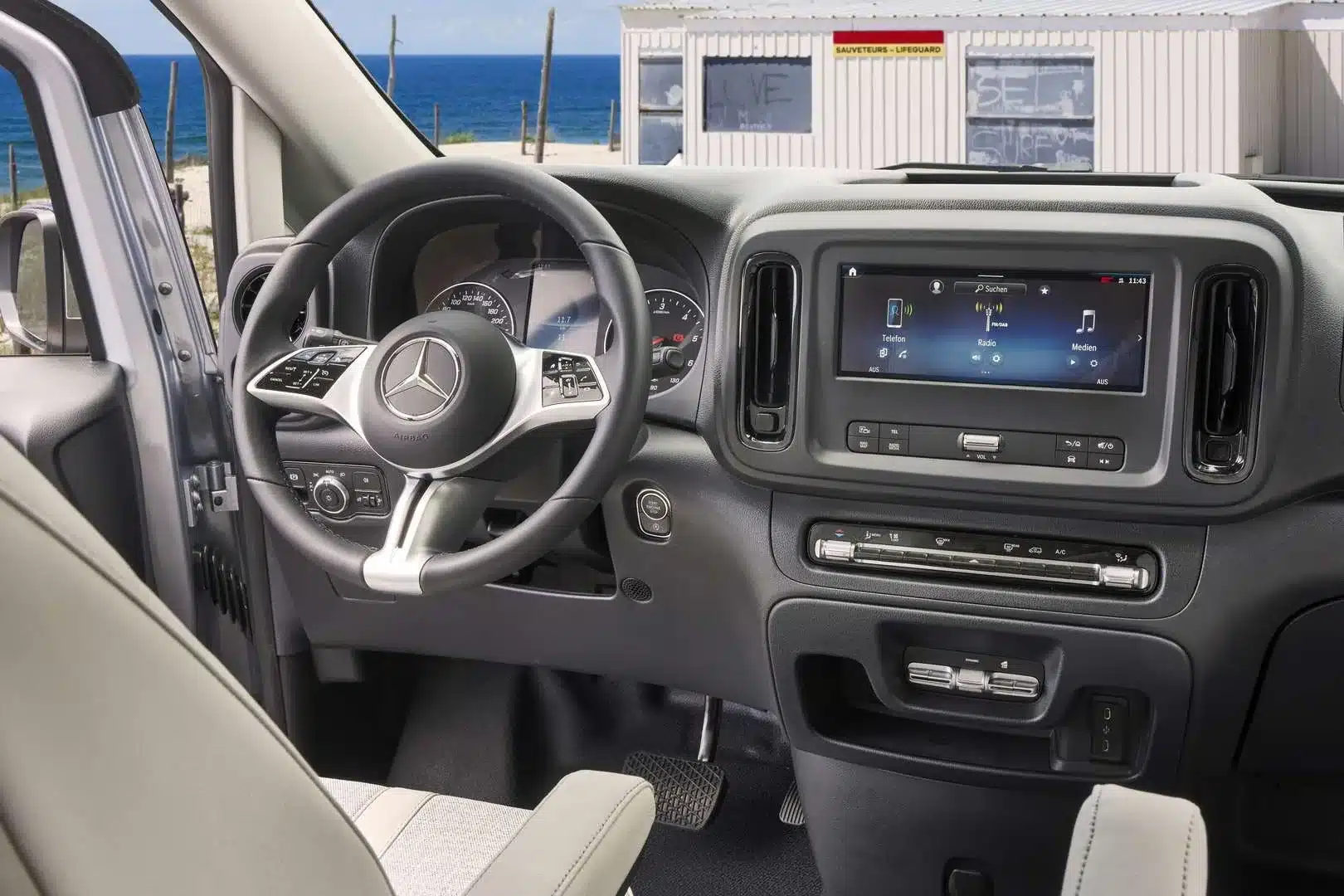 Innenansicht des Cockpits eines Westfalia Jules Verne Campervans mit Mercedes-Lenkrad und Infotainmentsystem, Blick auf das Meer im Hintergrund