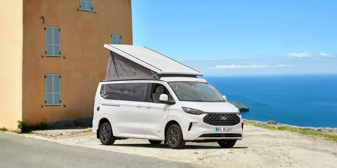 Weißer Westfalia Kelsey Campervan mit geöffnetem Aufstelldach steht vor einem Haus mit Blick auf das Meer