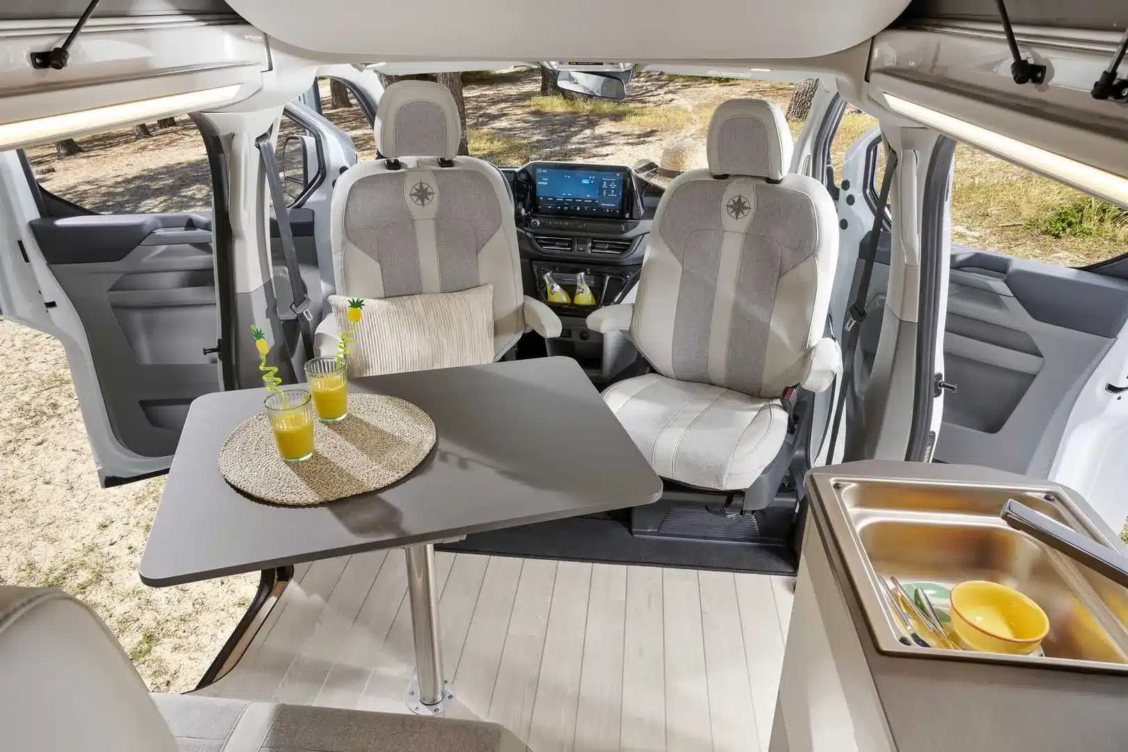 Innenansicht des Westfalia Kelsey Campervans mit drehbaren Vordersitzen, Tisch, Küchenzeile und geöffneter Schiebetür