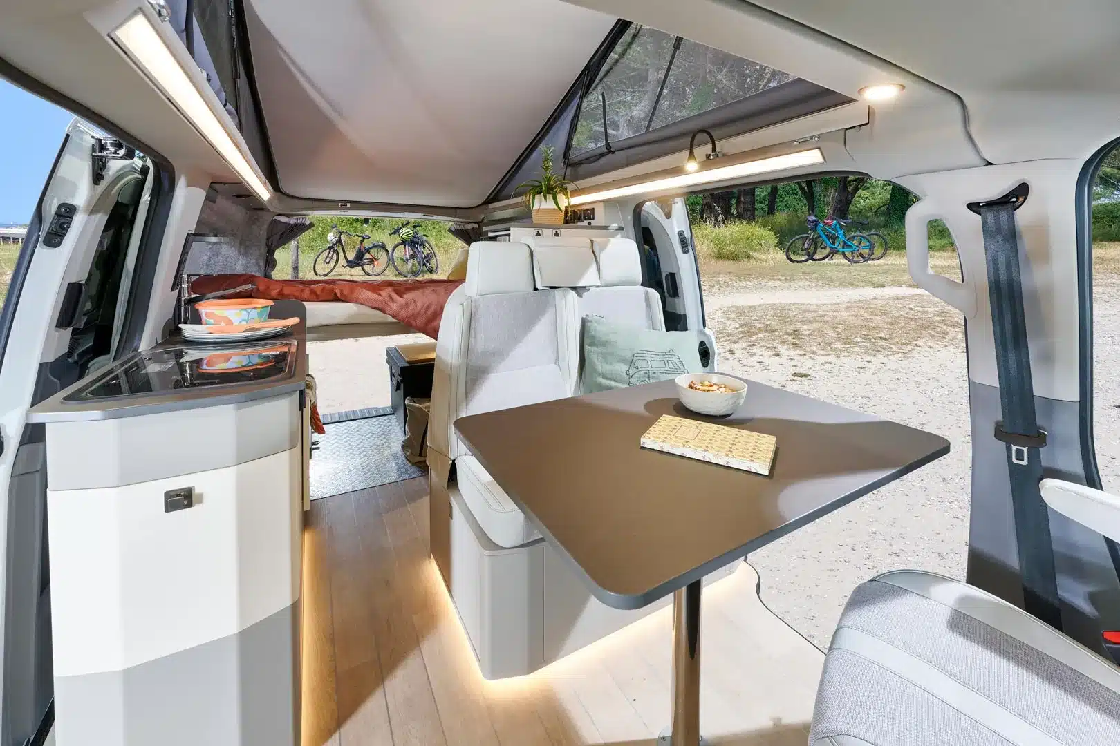 Innenansicht des Westfalia Kipling Campervans mit ausklappbarem Querschläferbett, Küchenzeile, Sitzgruppe und Blick nach draußen