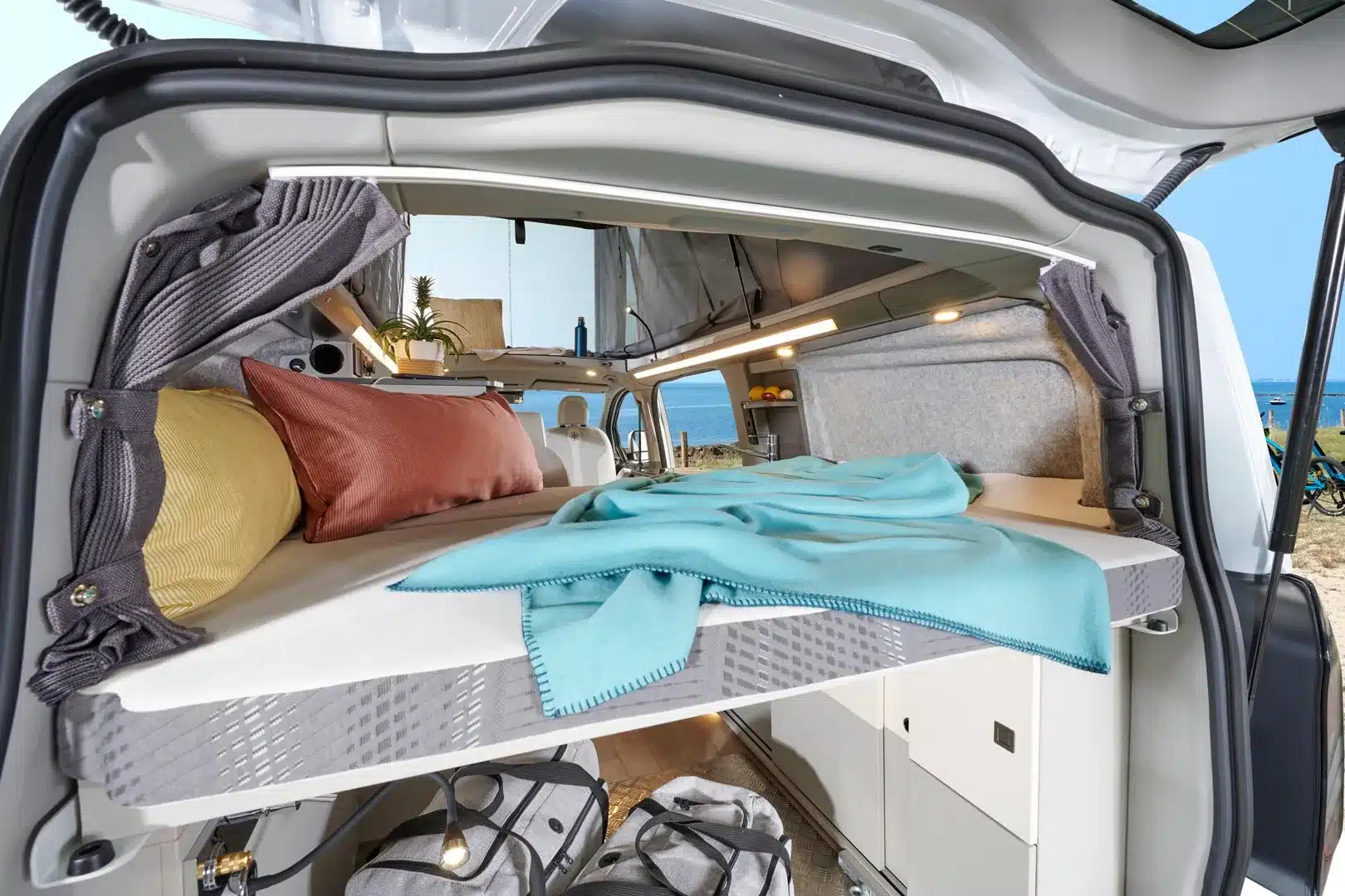 Blick in den Westfalia Kipling Campervan mit ausgeklapptem Querschläferbett, Stauraum und moderner Innenausstattung am Strand.