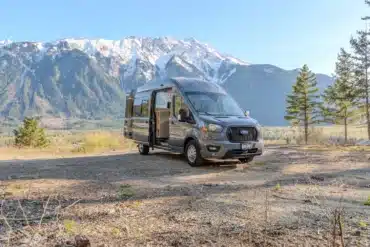 Ford Transit Campervan Willow Van Conversion mit offener Schiebetür in der Natur vor verschneiten Bergen