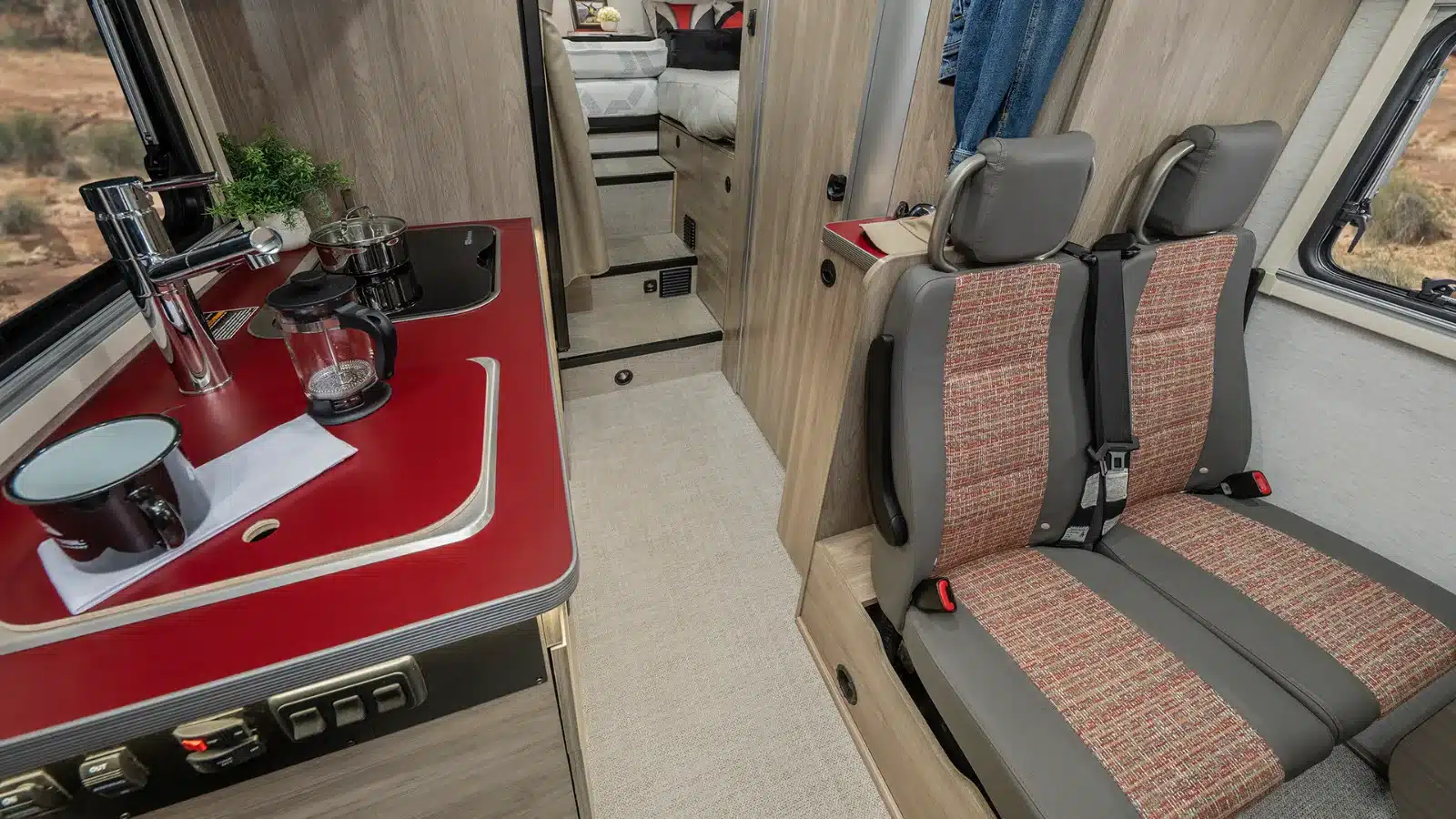 Blick in den Innenraum eines Winnebago EKKO mit roter Küchenarbeitsplatte, Spüle, Induktionskochfeld, Sitzbank und Blick auf das Bett im Hintergrund