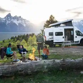 Winnebago Solis Pocket Campervan mit aufgestelltem Dach, Familie am Lagerfeuer, Berge im Hintergrund