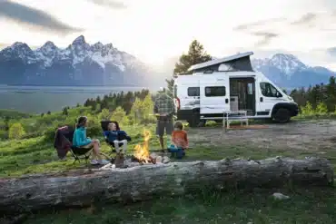 Winnebago Solis Pocket Campervan mit aufgestelltem Dach, Familie am Lagerfeuer, Berge im Hintergrund