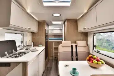 Blick in den Innenraum eines Alkoven-Wohnmobils mit Küchenzeile, Sitzgruppe und Stauraum