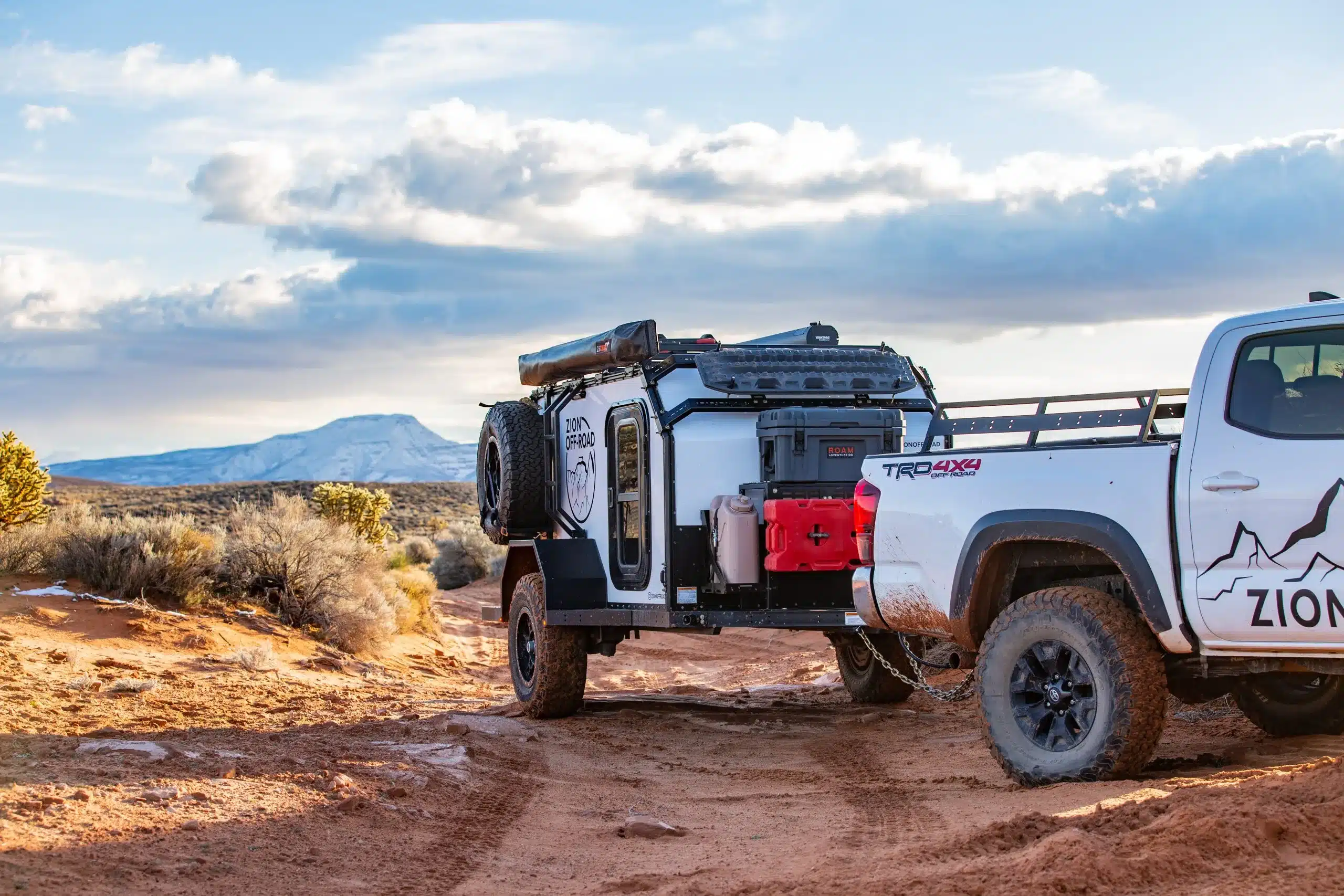 Zion Off-Road Z1-Base Trailer an einem Pickup auf einer Offroad-Piste in wüstenartiger Landschaft mit Bergen im Hintergrund