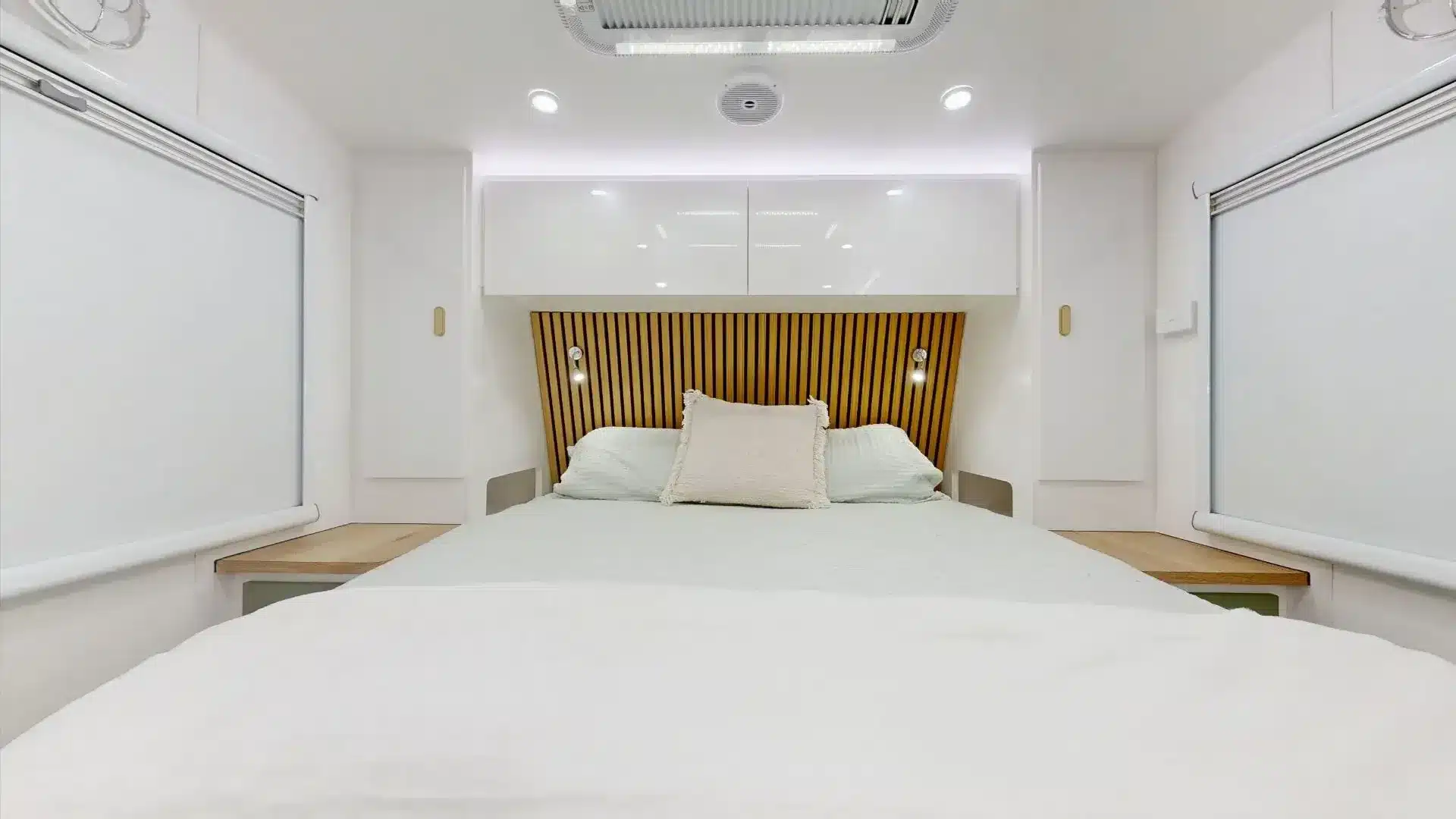 Innenansicht des Master-Queen-Betts im Zeus Quad Bunk Caravan mit Holz-Elementen und weißen Schränken