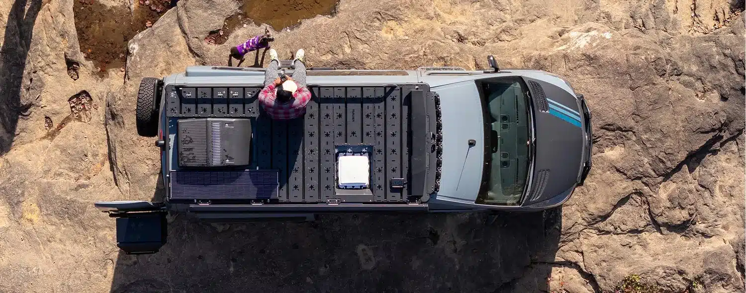 Draufsicht auf einen 2026 Beast Mode OG Offroad-Campervan, geparkt auf Felsen, eine Person sitzt auf dem Dach