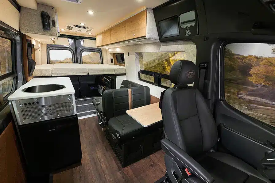 Innenraum des 2026 Beast Mode OG Offroad-Kastenwagens mit Sitzen, Tisch, Küche und Querbett im Heck.