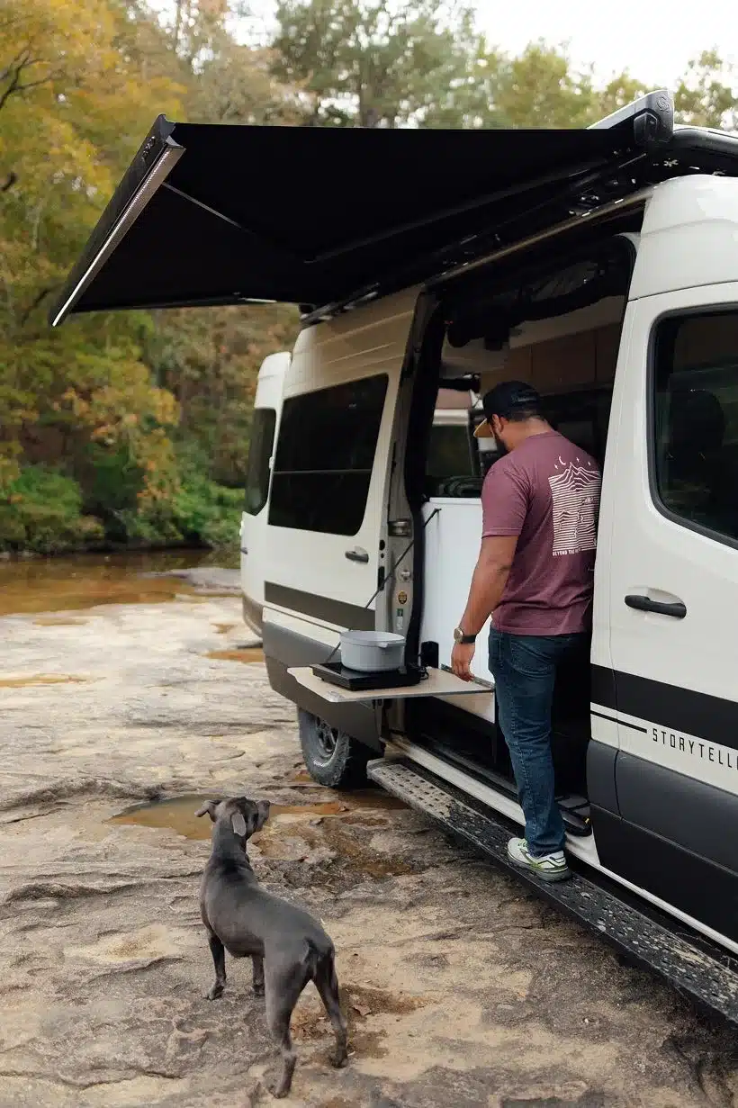 Seitenansicht des Classic MODE XO Campervans mit ausgefahrener Markise, Outdoor-Kochbereich und Hund im Vordergrund.
