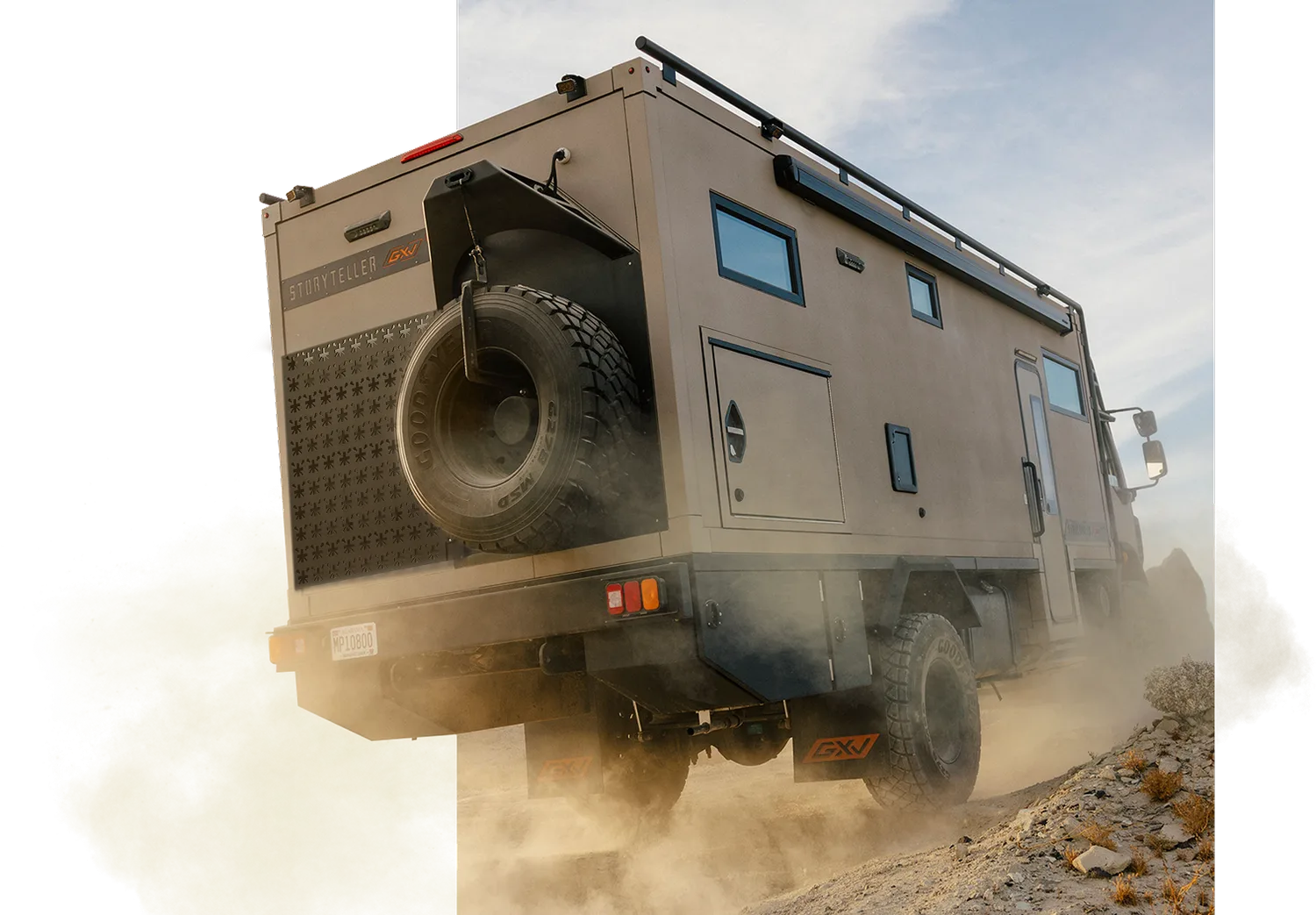 Heckansicht des 2026 GXV Epic Expeditions-LKWs mit Ersatzrad im Gelände, aufgewirbelter Staub zeigt Offroad-Fähigkeit.