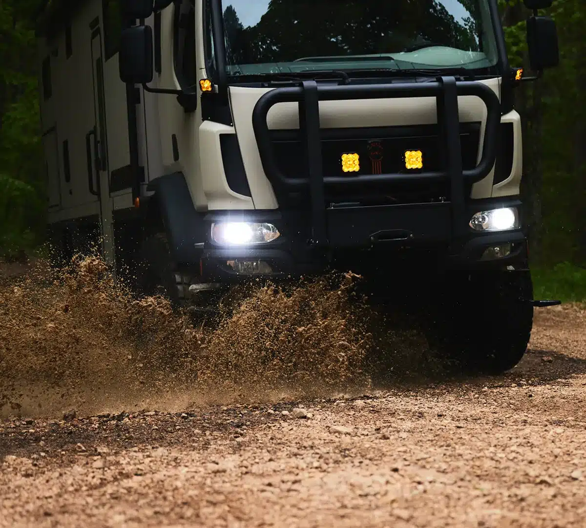 Frontansicht des 2026 GXV Epic Expeditionsfahrzeugs, wie es auf einer schlammigen Piste durch den Wald fährt.