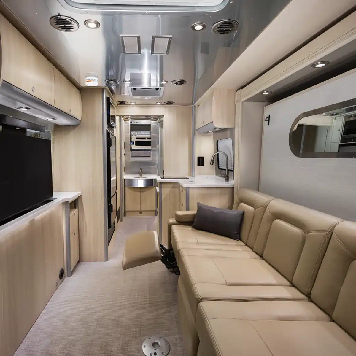 Der Wohnbereich des Airstream Atlas 2026 mit beiger Ledercouch, Küchenzeile, TV und modernen Einbaumöbeln.