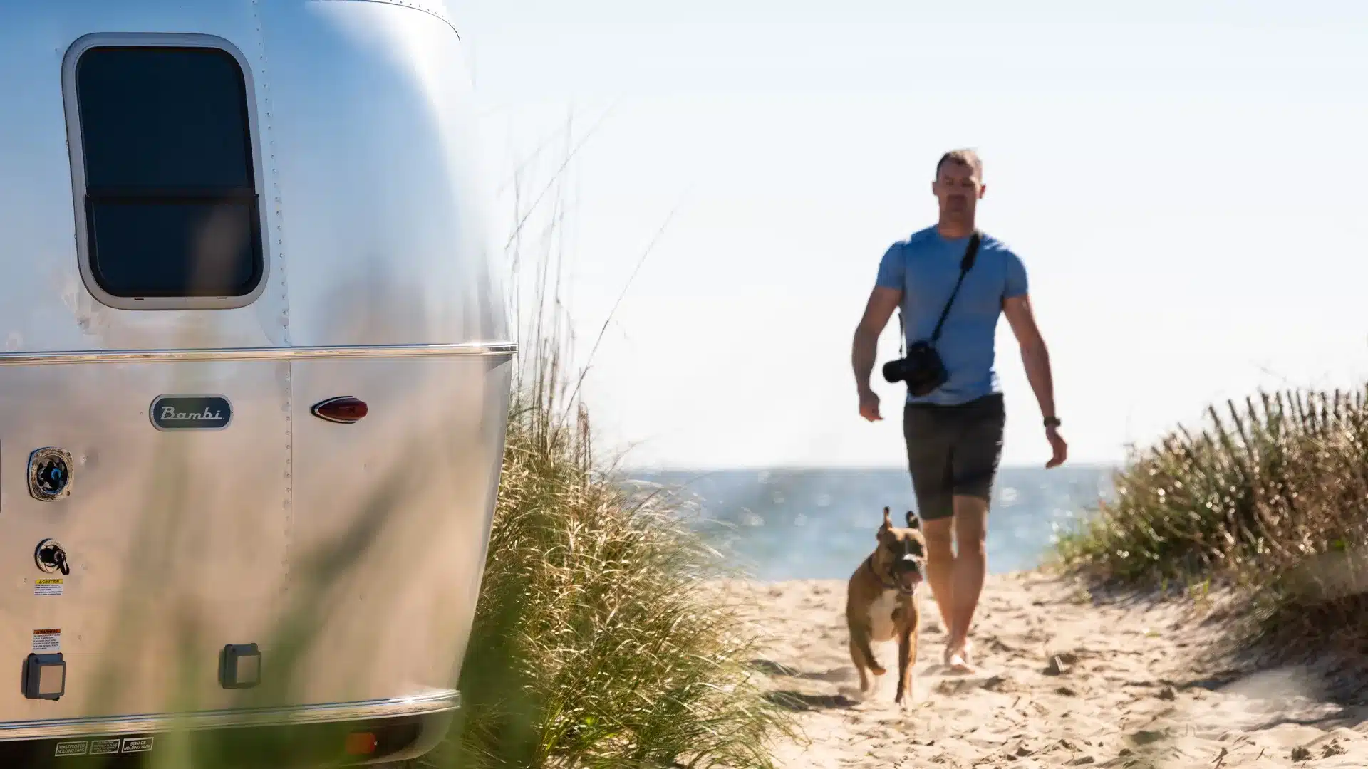 Airstream Bambi 16RB Wohnwagen am Strand mit Mann und Hund im Hintergrund
