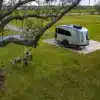 Airstream Basecamp 20Xe Wohnwagen auf einer Rasenfläche mit Baumschaukel, isoliert in der Natur, Seitenansicht.