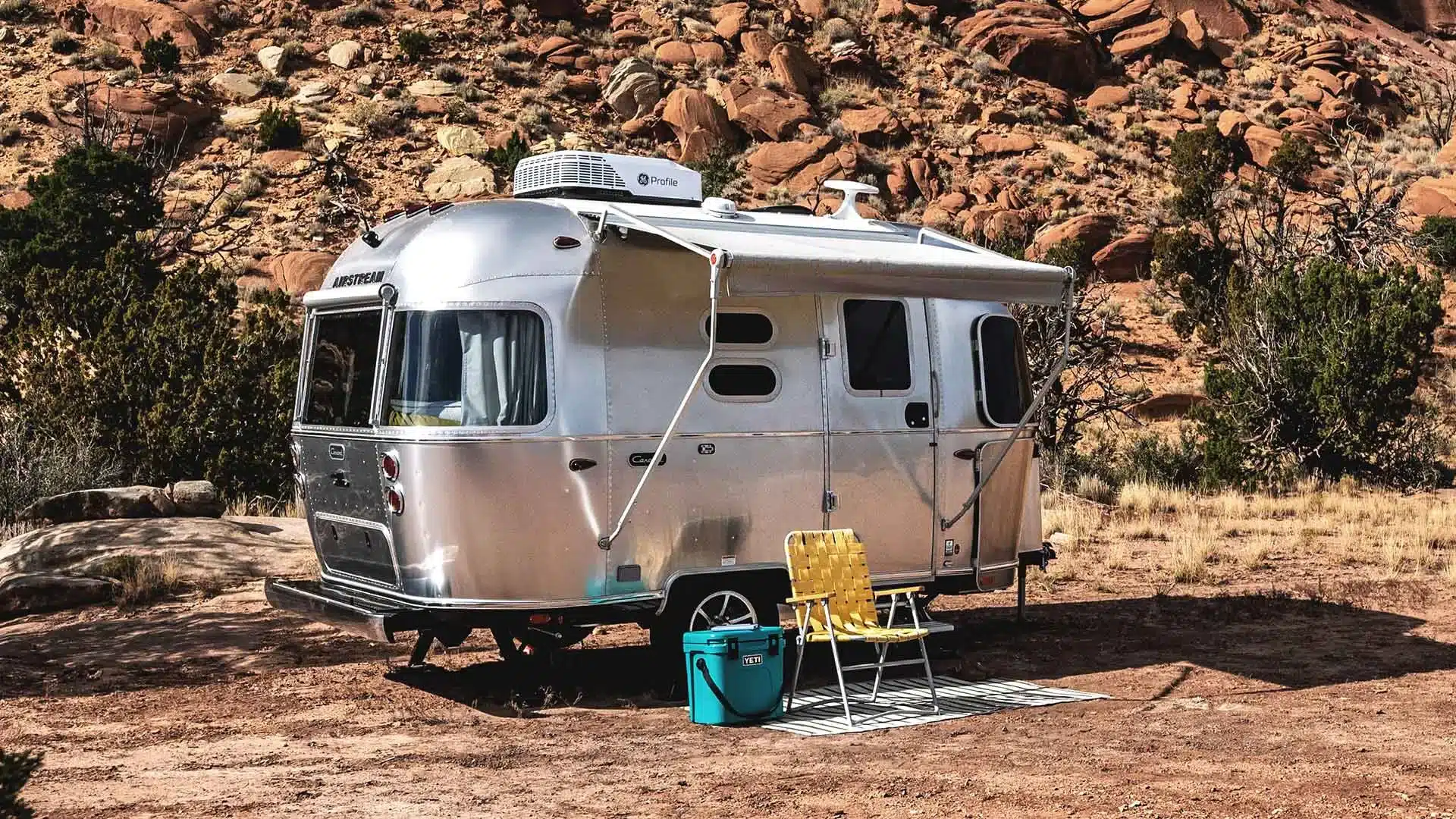 Airstream Caravel 16RB 2026 Campinganhänger mit ausgefahrener Markise und Campingmöbeln in wüstenartiger Landschaft.