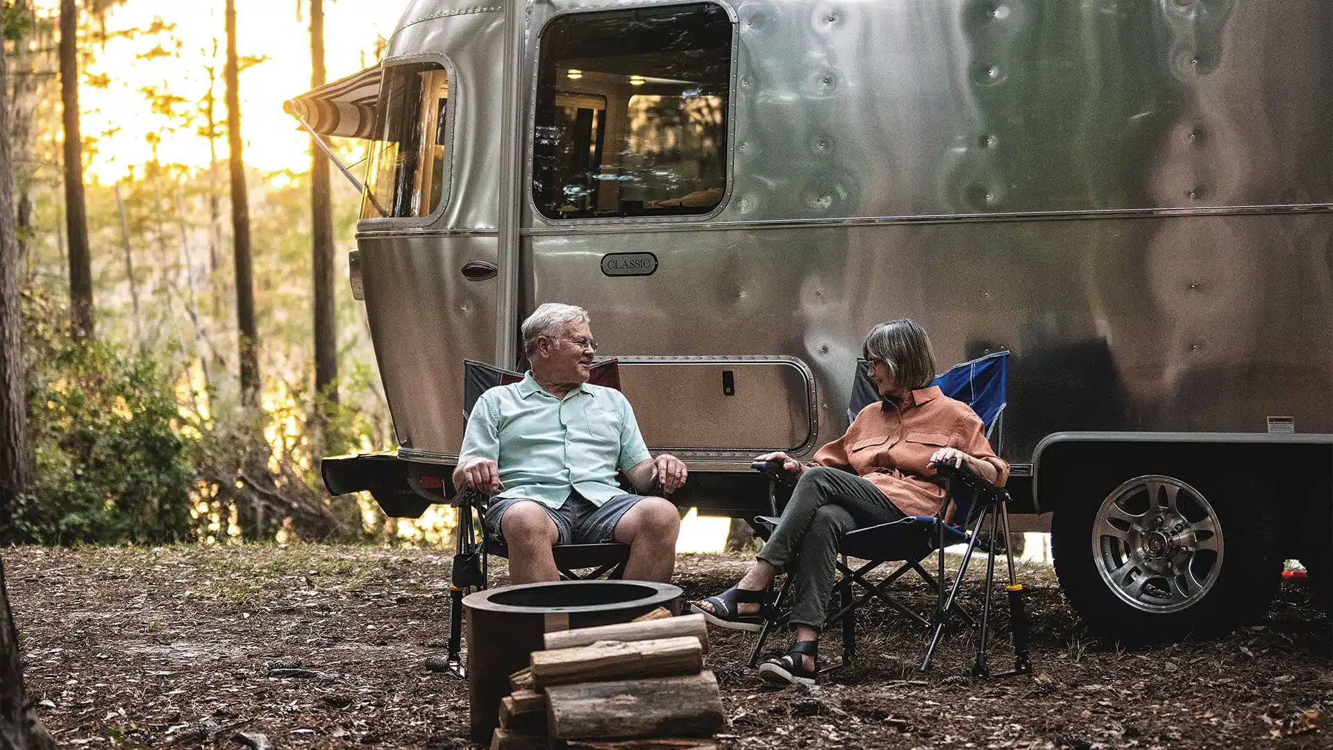 Airstream Classic 2026 Wohnwagen mit zwei Menschen beim Camping am Waldrand
