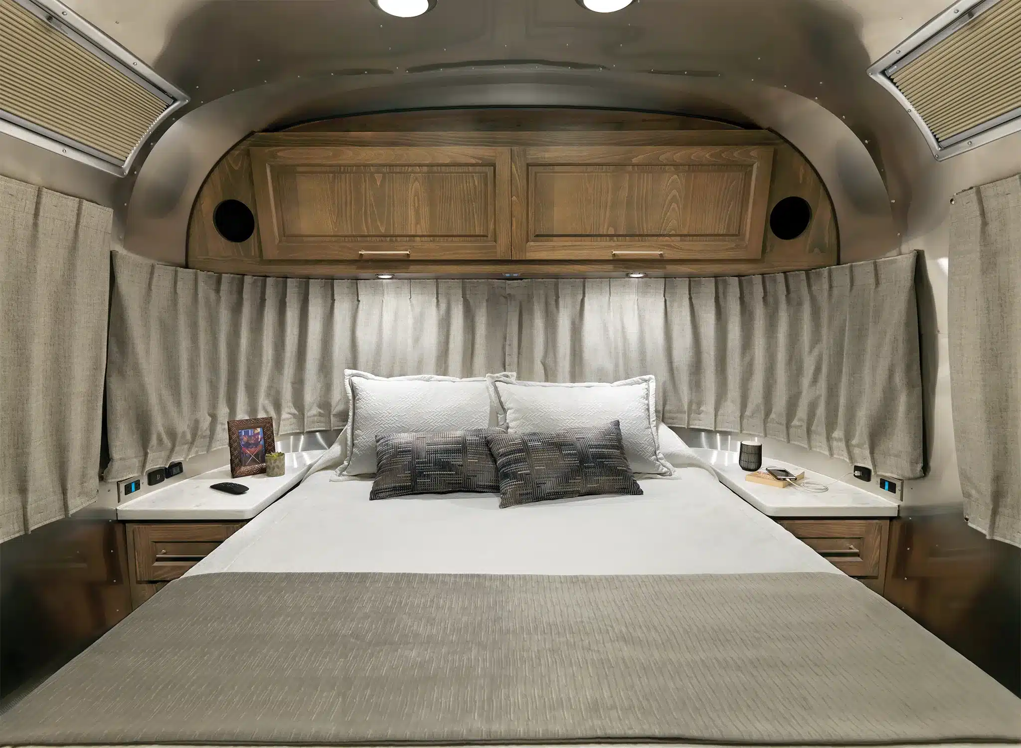 Schlafbereich mit großem Bett, Holzschränken und Vorhängen im Airstream Classic 2026 Wohnwagen.