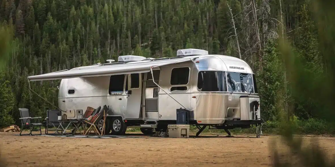 Airstream Flying Cloud 30FB Bunk Travel Trailer mit ausgefahrener Markise und Campingmöbeln im Wald