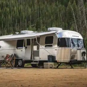Airstream Flying Cloud 30FB Bunk Travel Trailer mit ausgefahrener Markise und Campingmöbeln im Wald