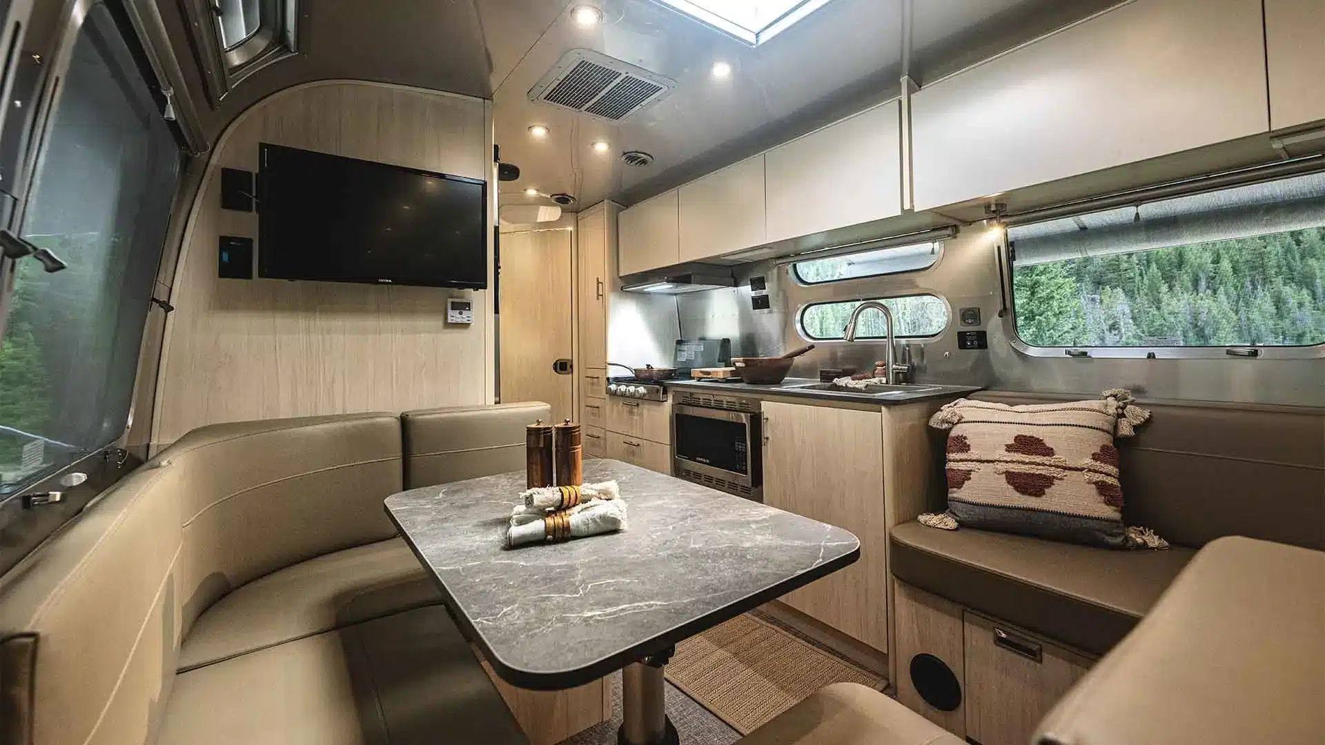 Modern eingerichteter Innenraum eines Airstream Flying Cloud 30FB Bunk Wohnanhängers mit Sitzgruppe, Esstisch, Sofa, Fernseher und Küchenzeile