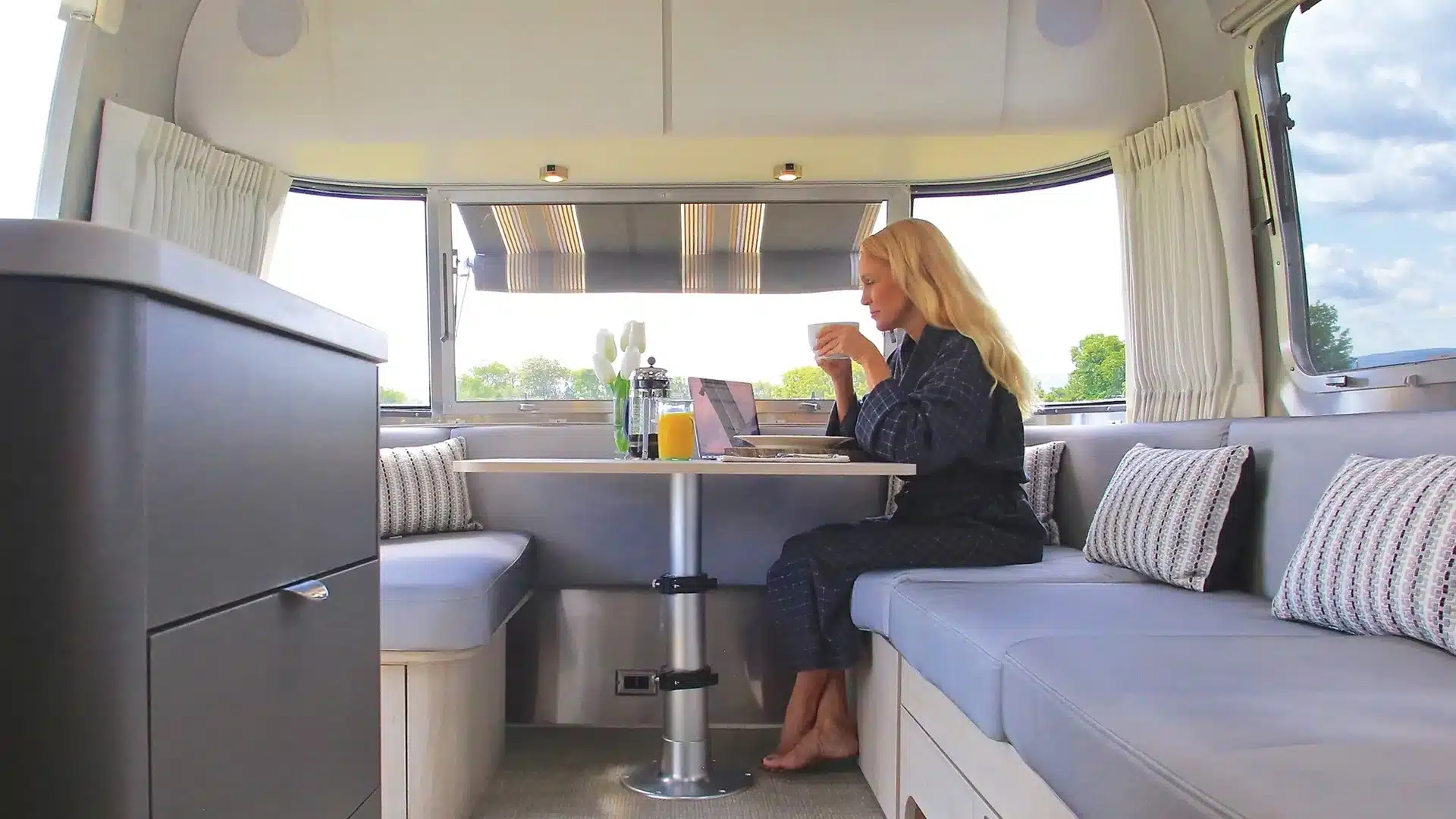 Frau am Tisch in der Sitzecke eines Airstream Globetrotter Wohnwagens beim Frühstück und Arbeiten am Laptop