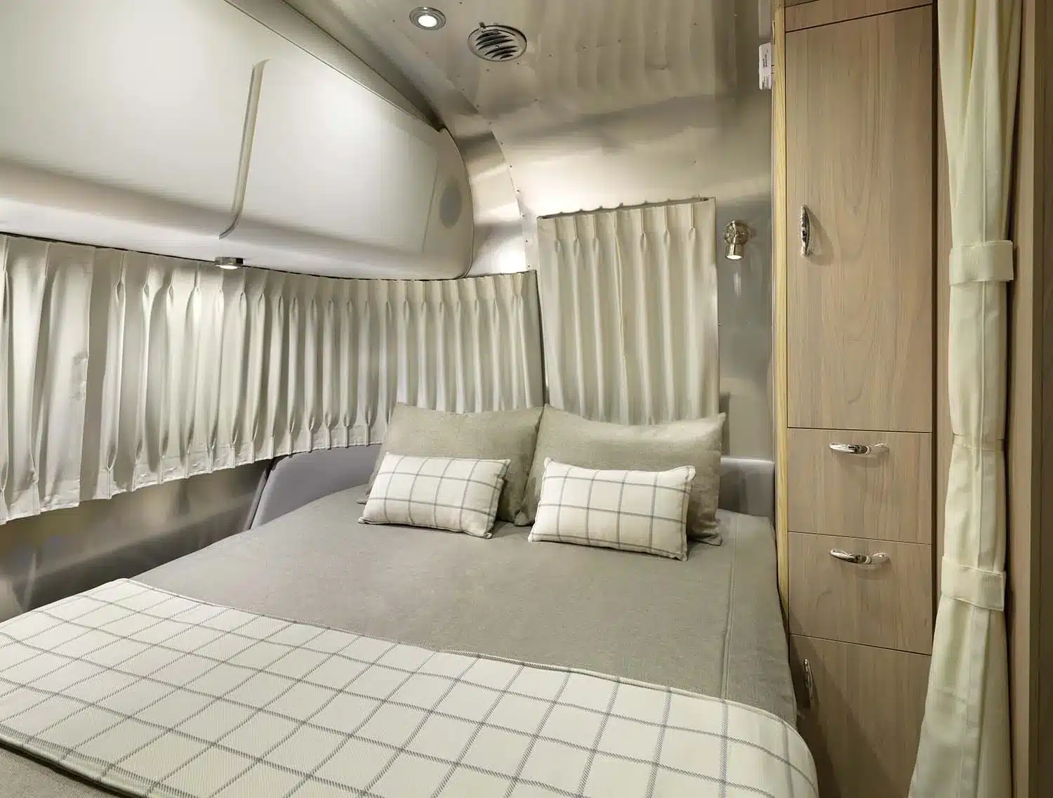 Schlafzimmer mit Doppelbett, Vorhängen und Schränken im Airstream Globetrotter Wohnanhänger